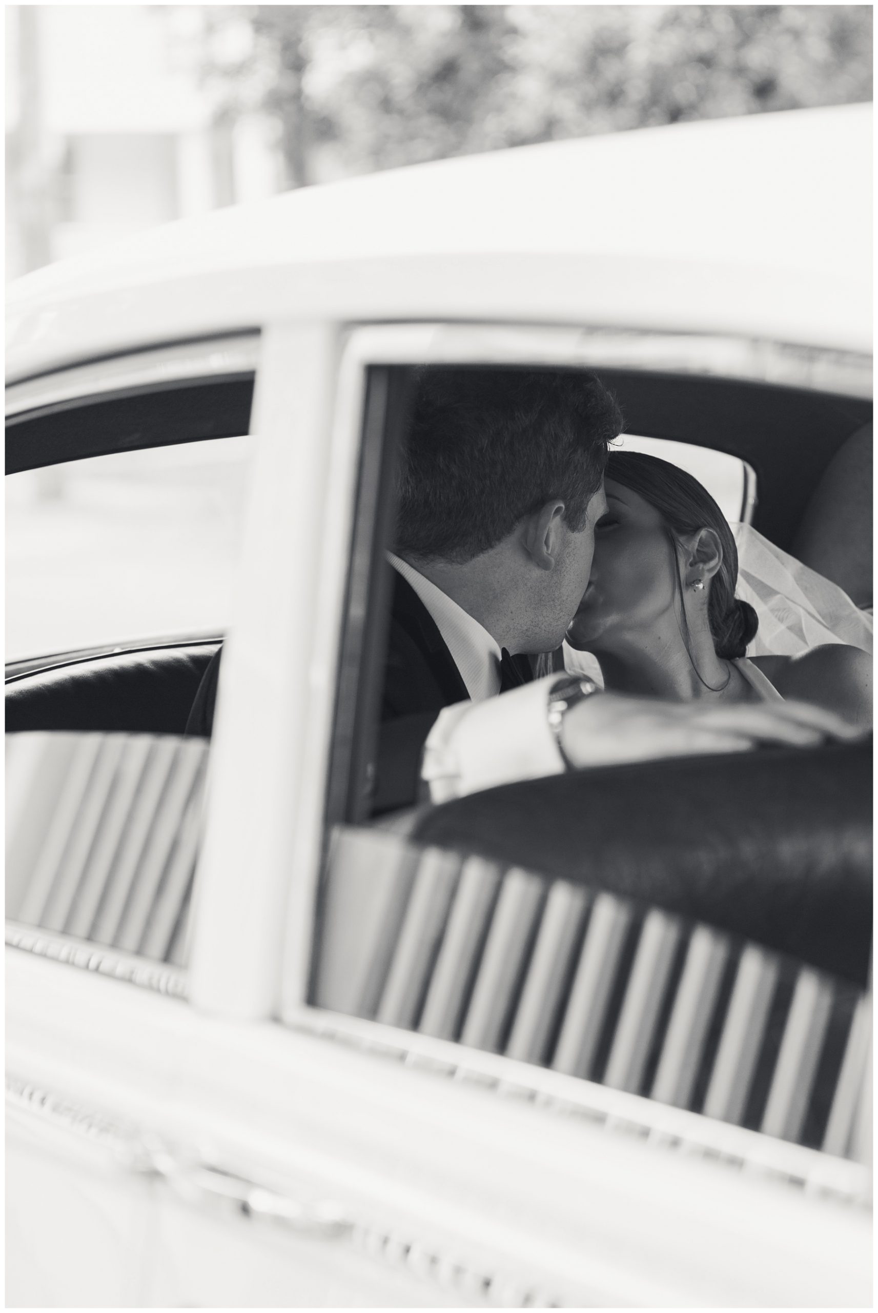 bride and groom kiss in back seat of classic white car in Charleston SC