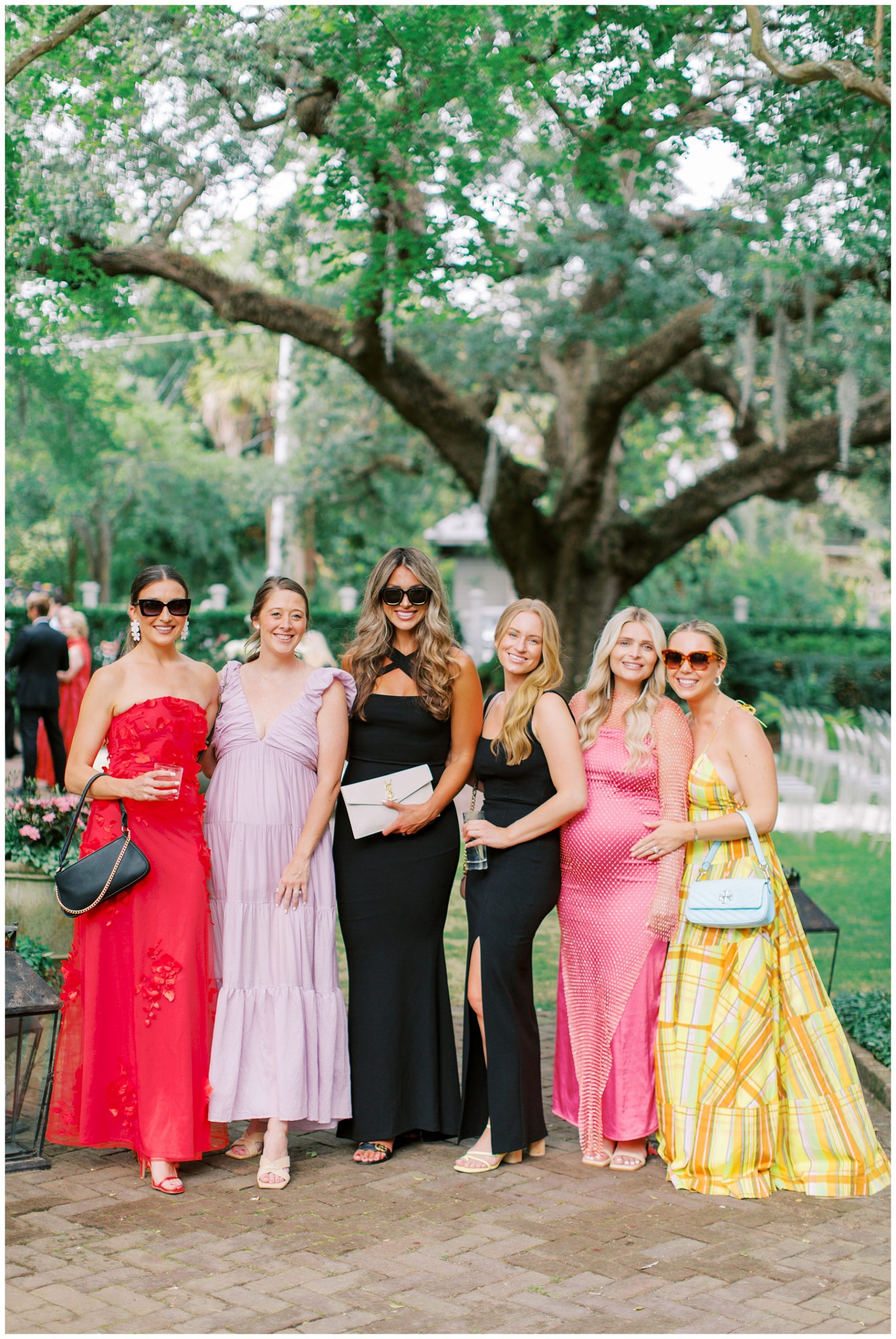wedding guests pose in cocktail dresses by large tree in South Carolina at the Governor Thomas Bennett House
