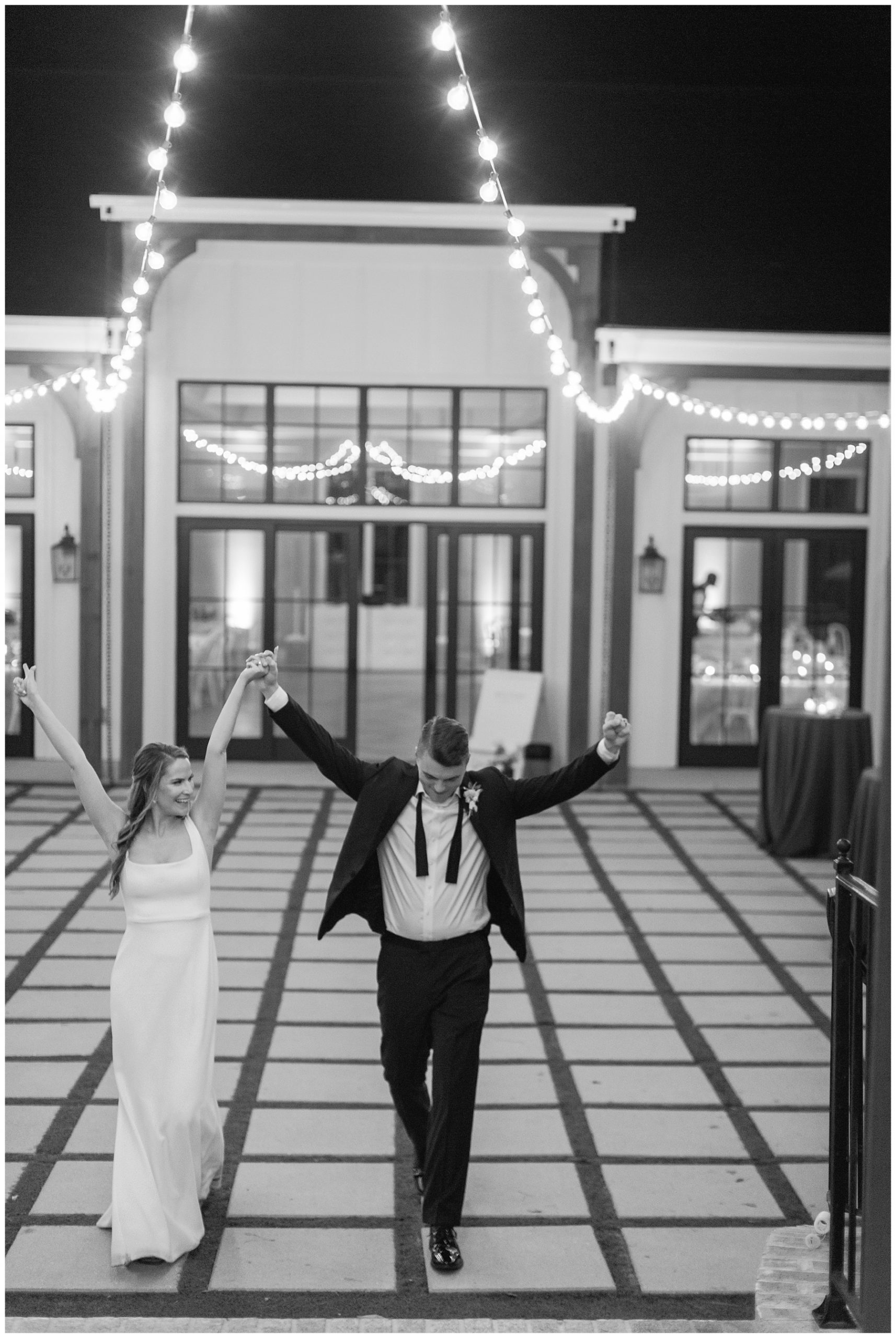 bride and groom hold hands cheering and walking across patio at The Bradford under patio lights 