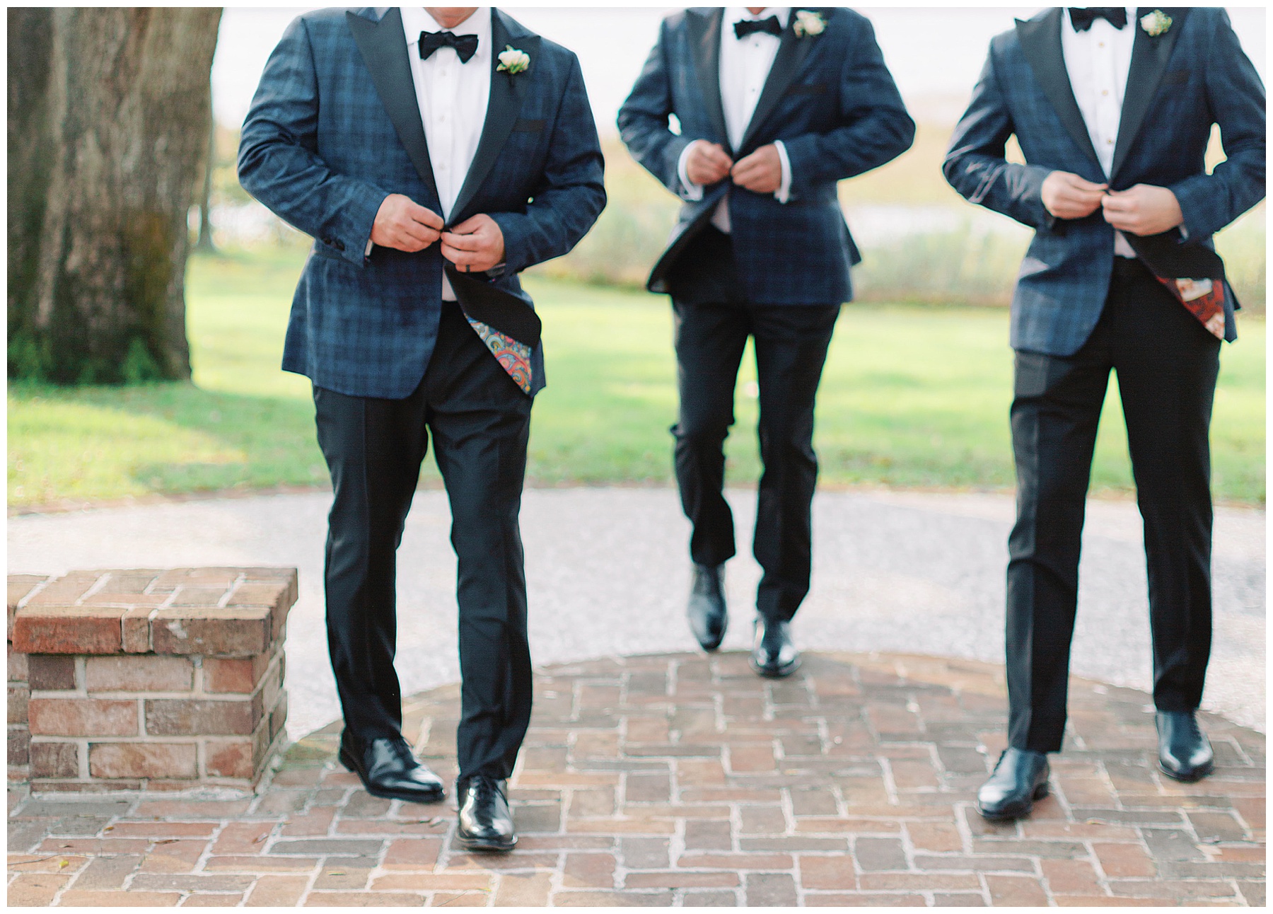 groomsmen walk on brick patio buttoning up plaid jacket at Lowndes Grove