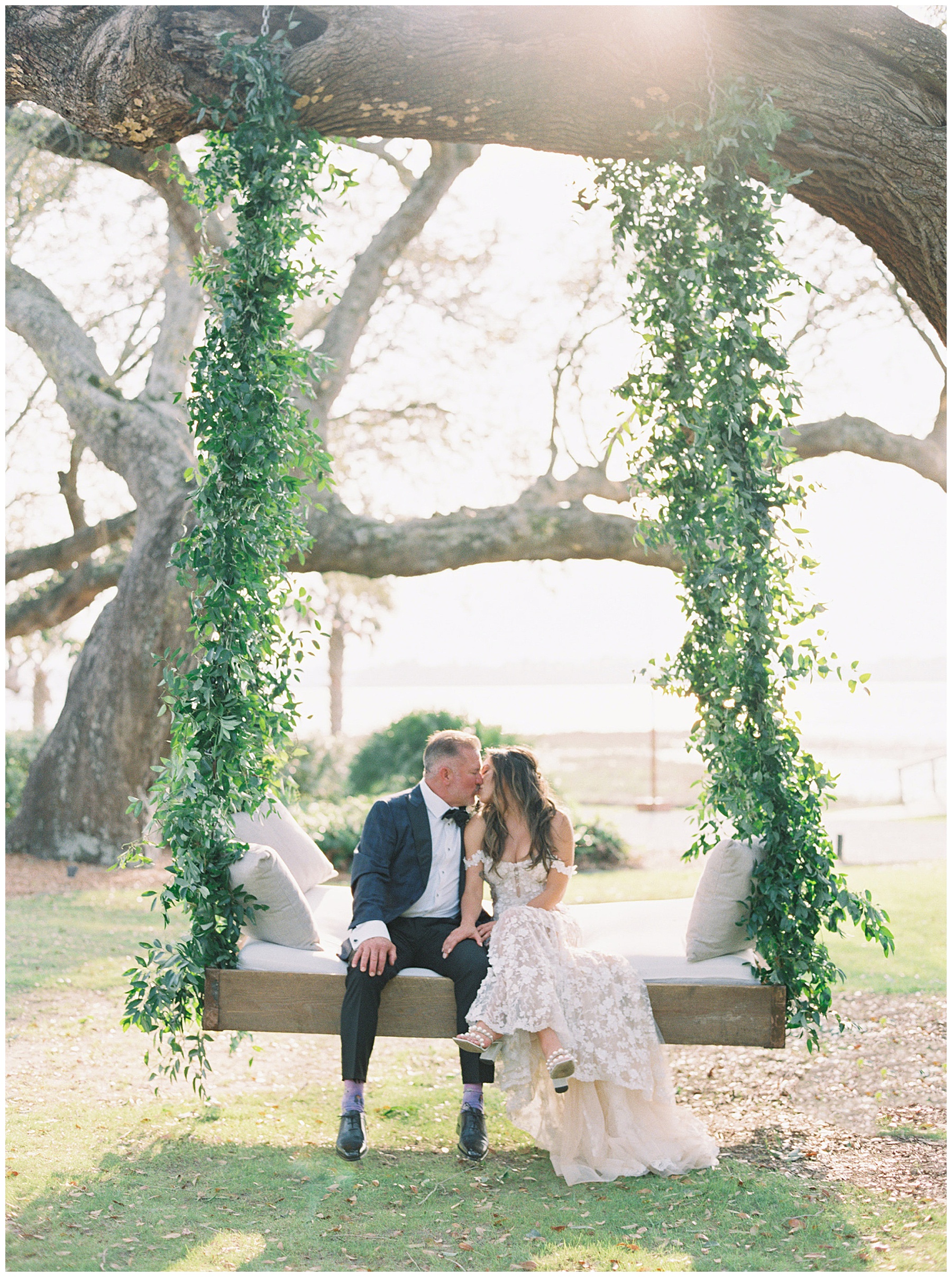 newlyweds kiss on swing with greenery and pillows at Lowndes Grove