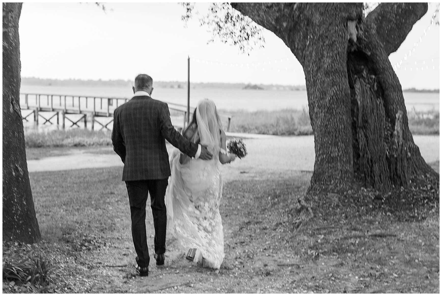 black and white photo of bride and groom walking under tress at Lowndes Grove
