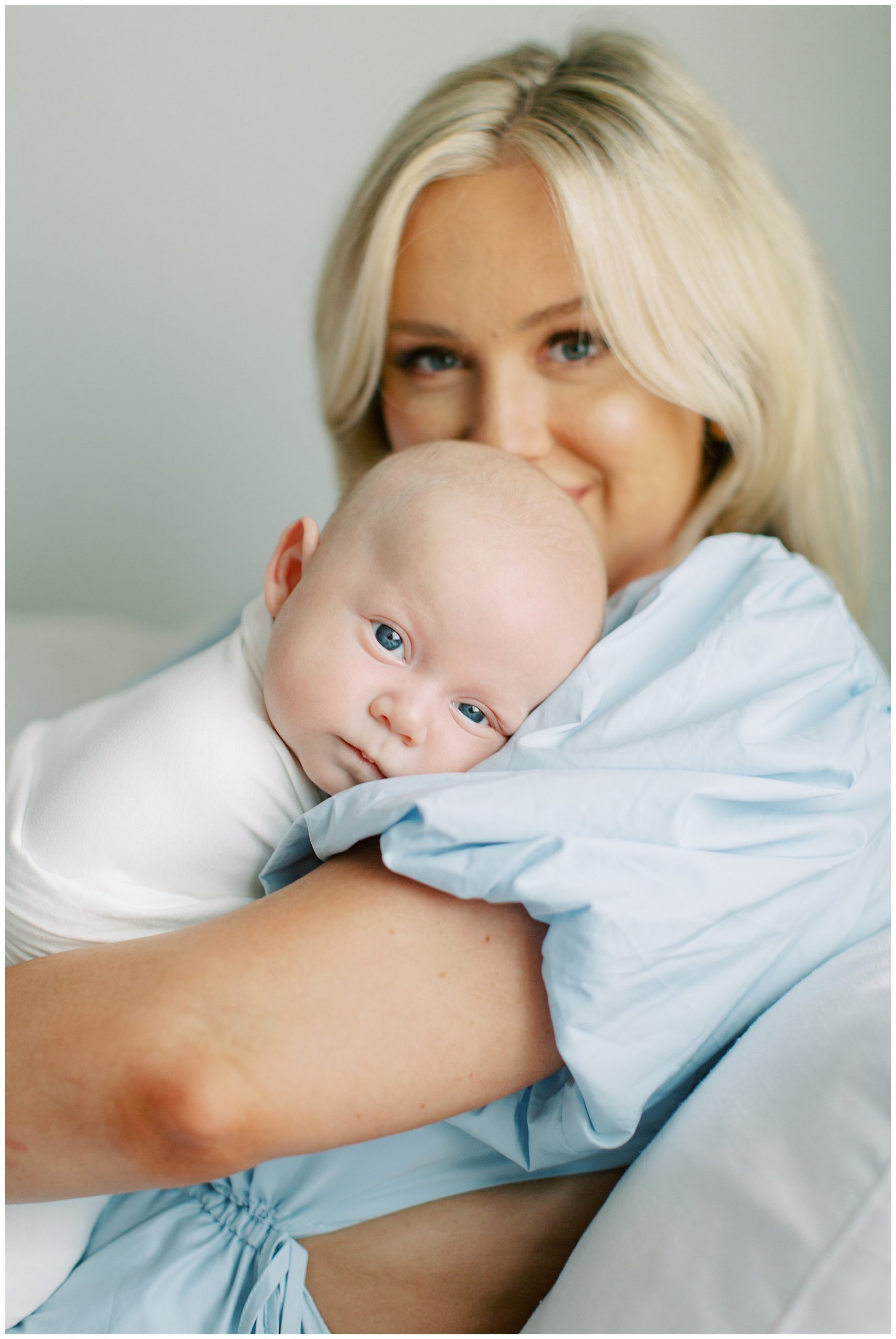 baby boy lays on mom's arm looking at camera with big lea eyes during Charlotte newborn session at home