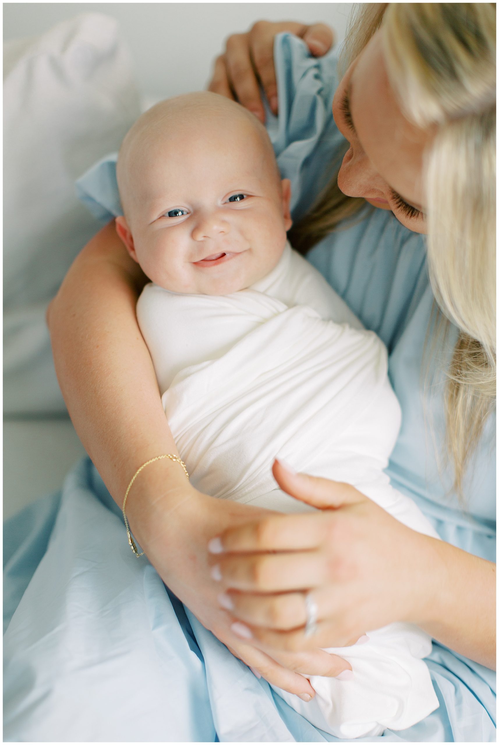 baby boy smiles while mom holds him during Charlotte newborn session at home