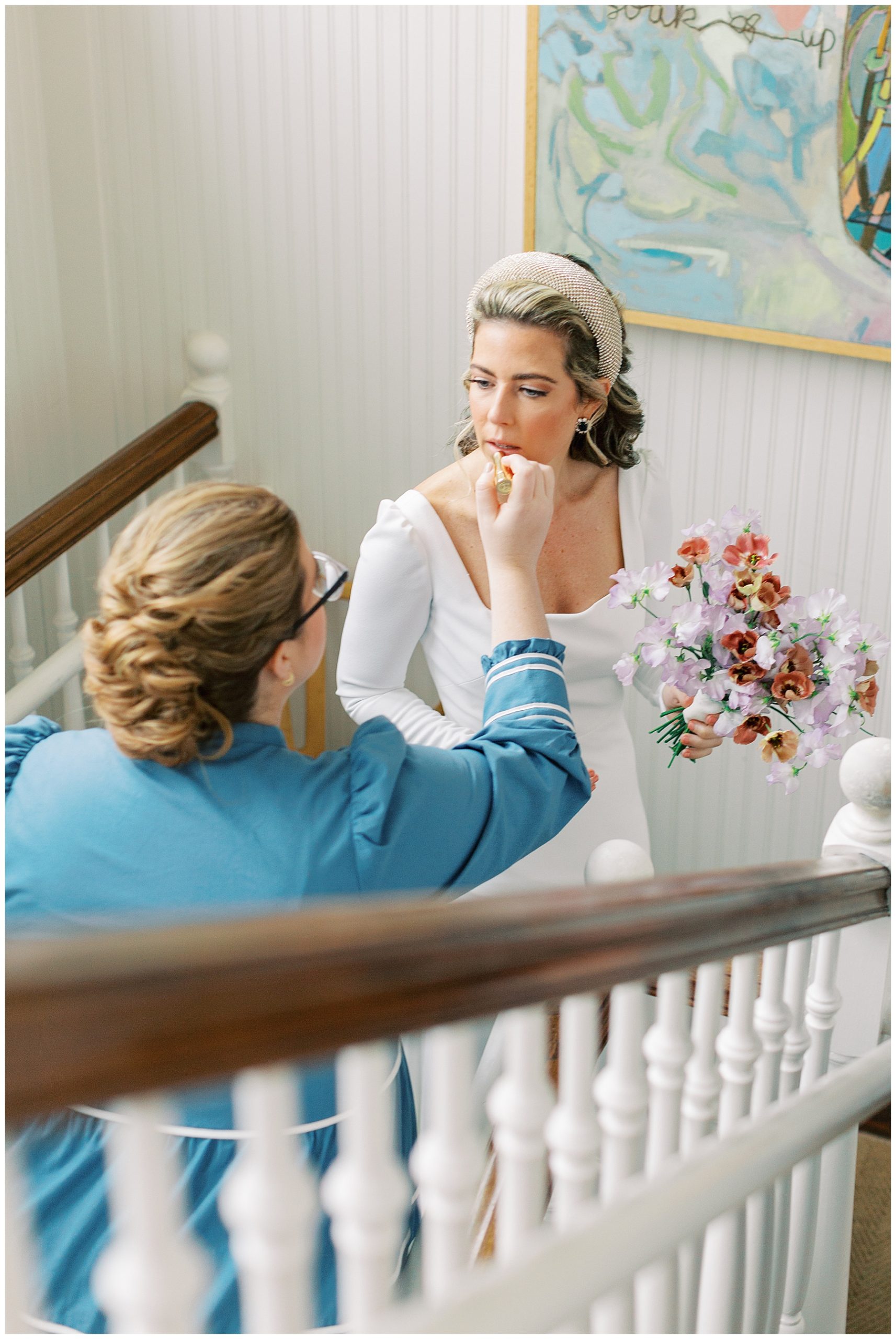 woman in blue dress helps bride blot lipstick on staircase inside the Post House Inn
