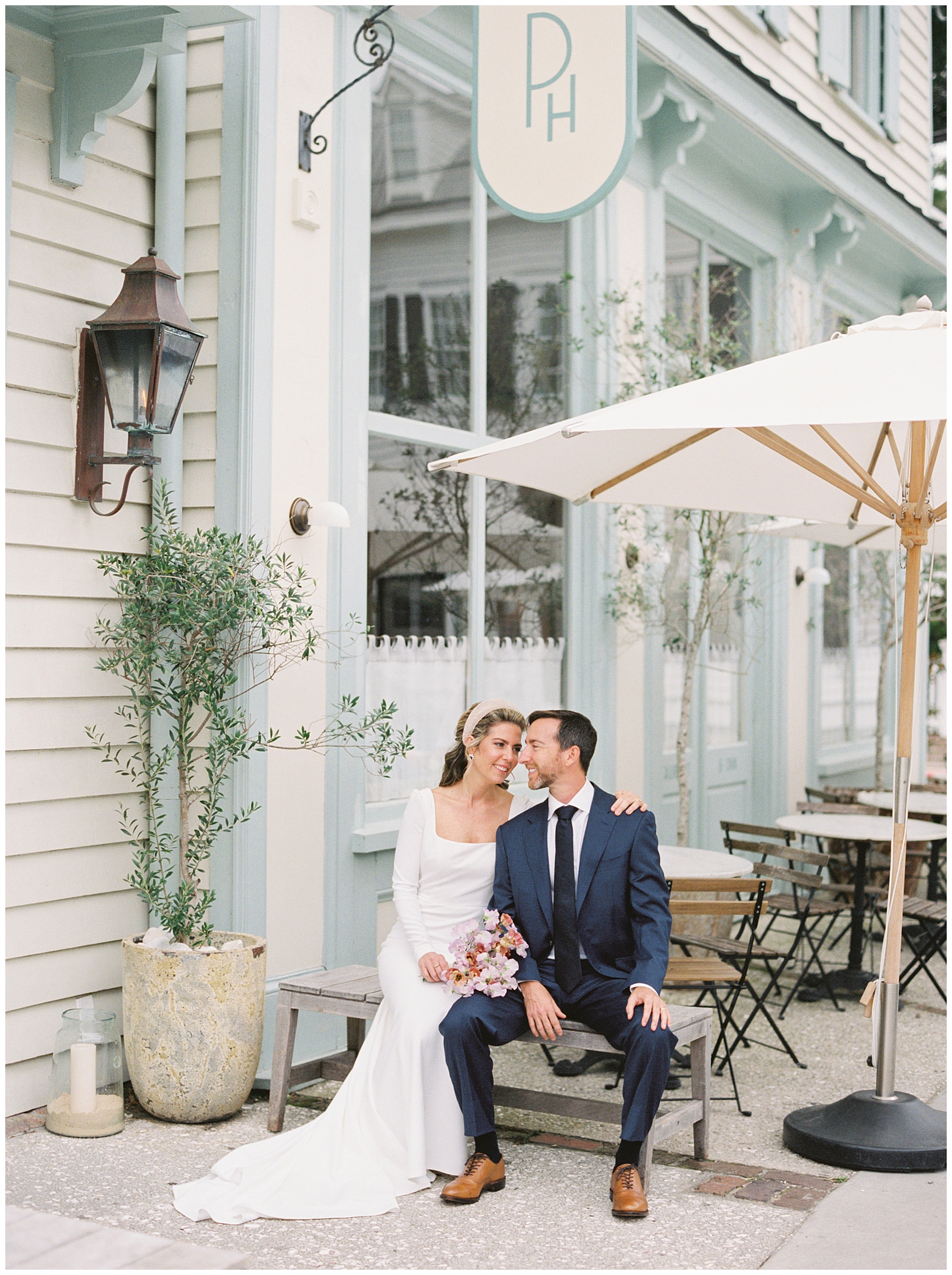 bride and groom sit on a bench outside but and white front of the Post House Inn