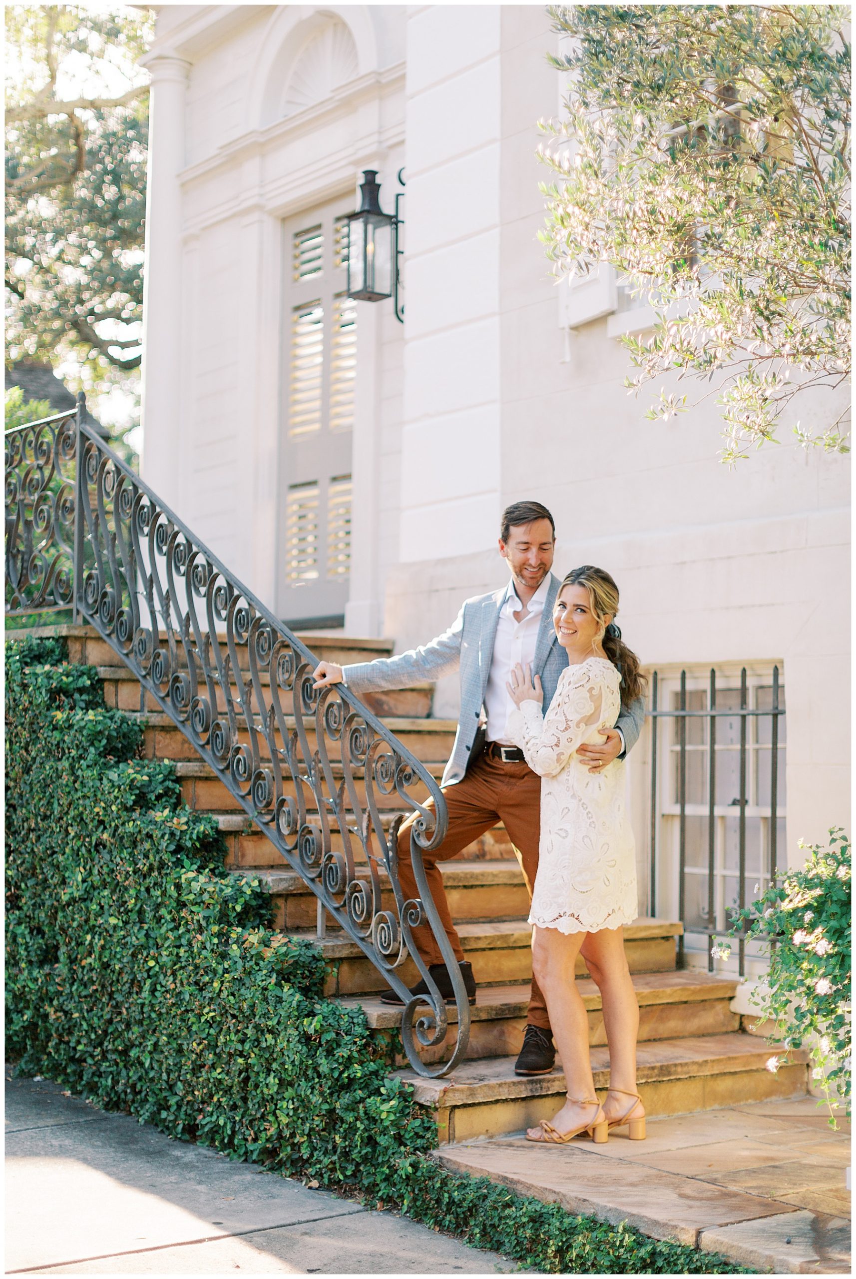 groom stands above bride on steps holding her to him outside Charleston SC home