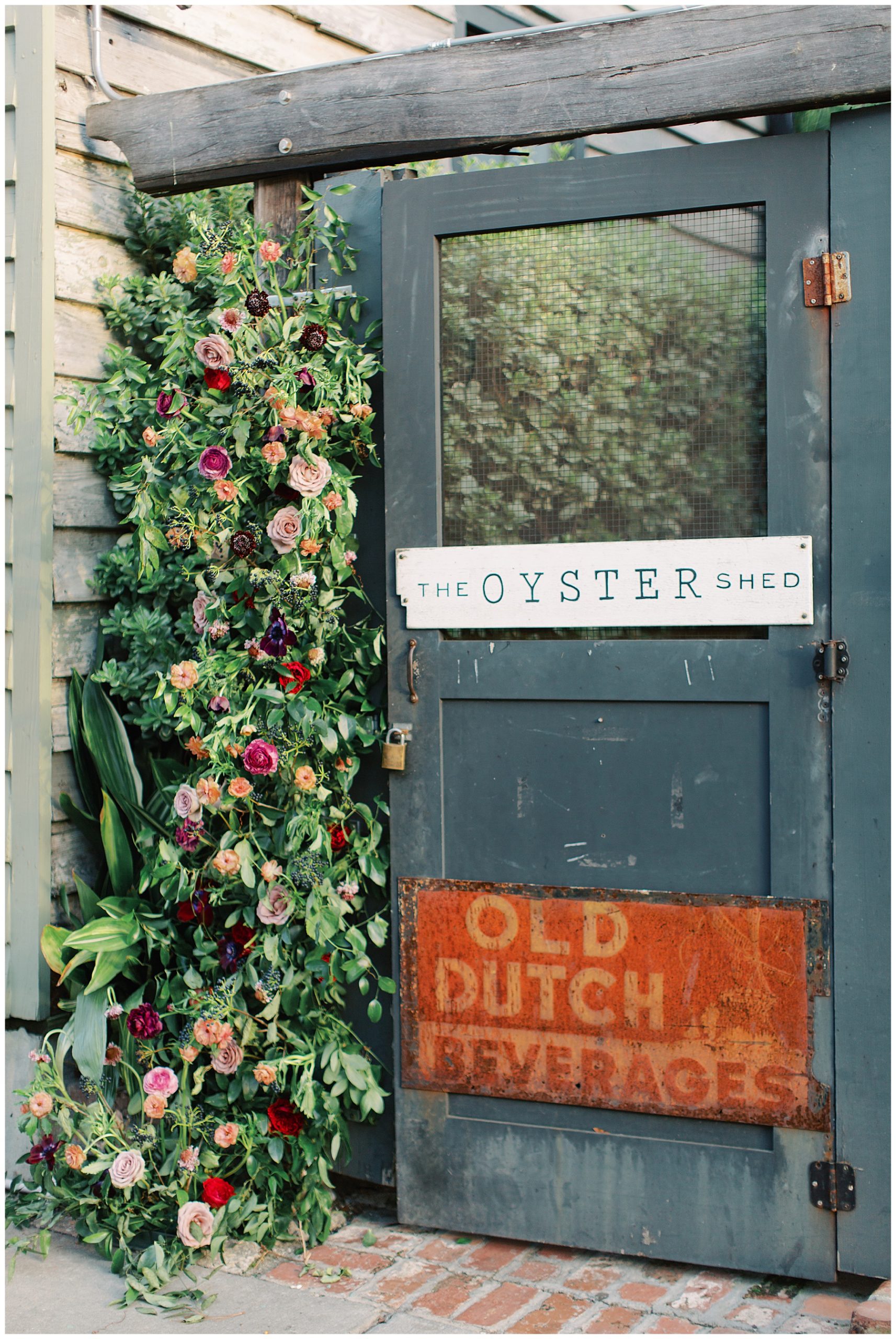 blue door with flowers coming down the side with a sign that says "The Oyster Shed" at Leon's Poultry & Oysters