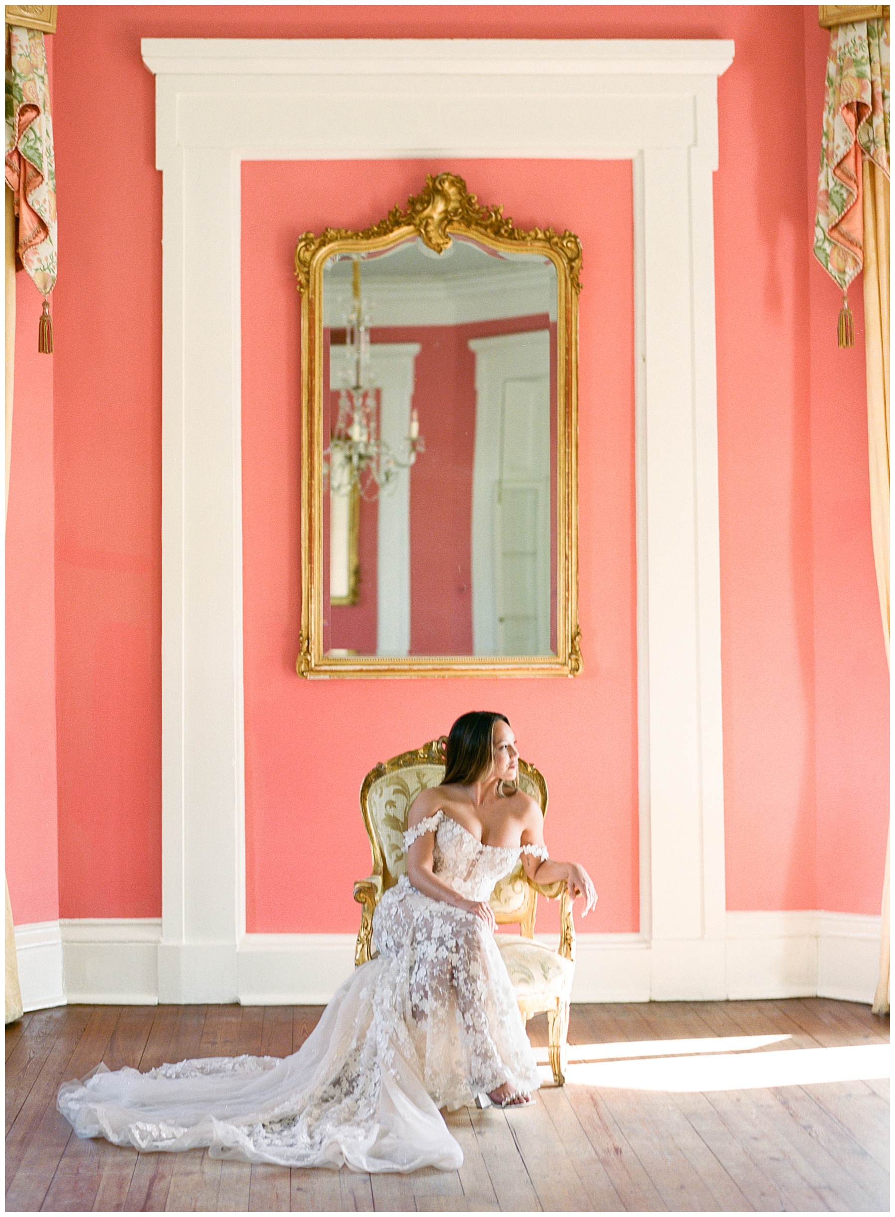 bride sits in gold framed chair under mirror inside coral room of the William Aiken House