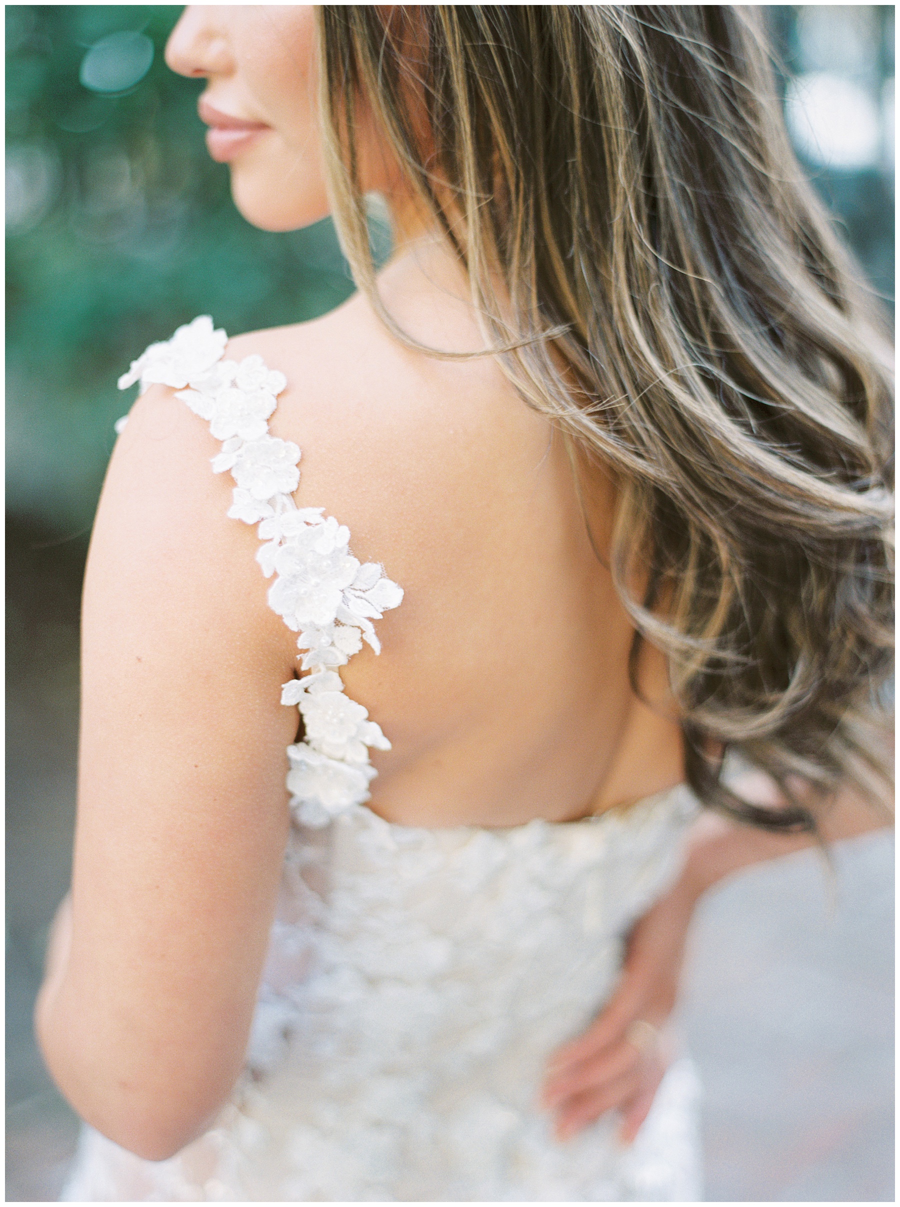 bride looks over shoulder with curled hair on her back and lace flowers on the straps