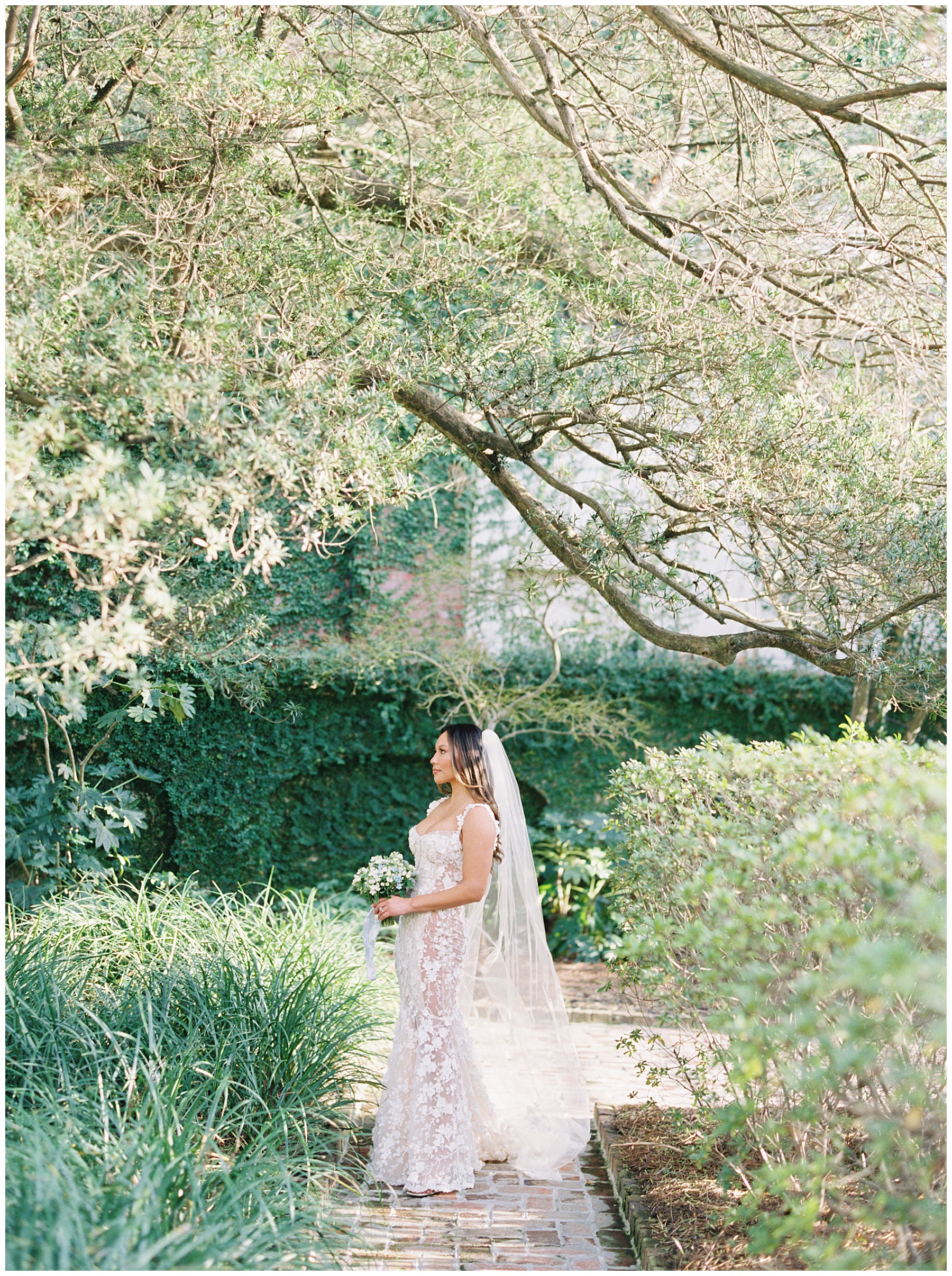 bride poses in gardens of the William Aiken House with her veil trailing behind her