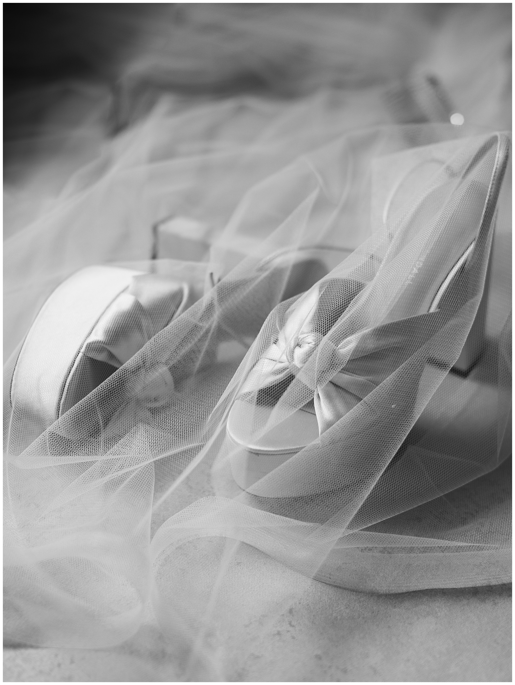 bride's wedding shoes with tied knots under veil in black and white photo 