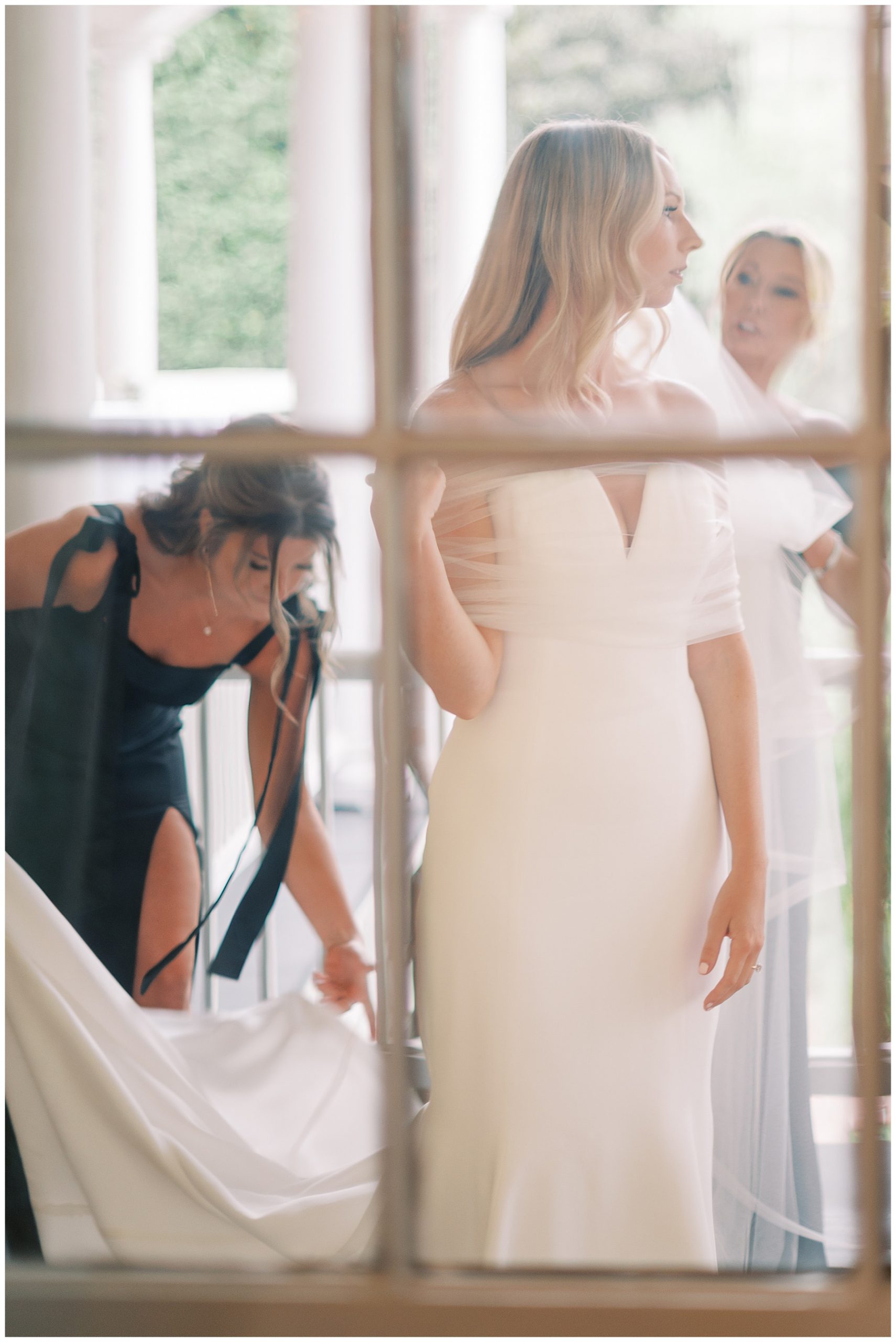 reflection of bridesmaid helping place bride's wedding dress on balcony 