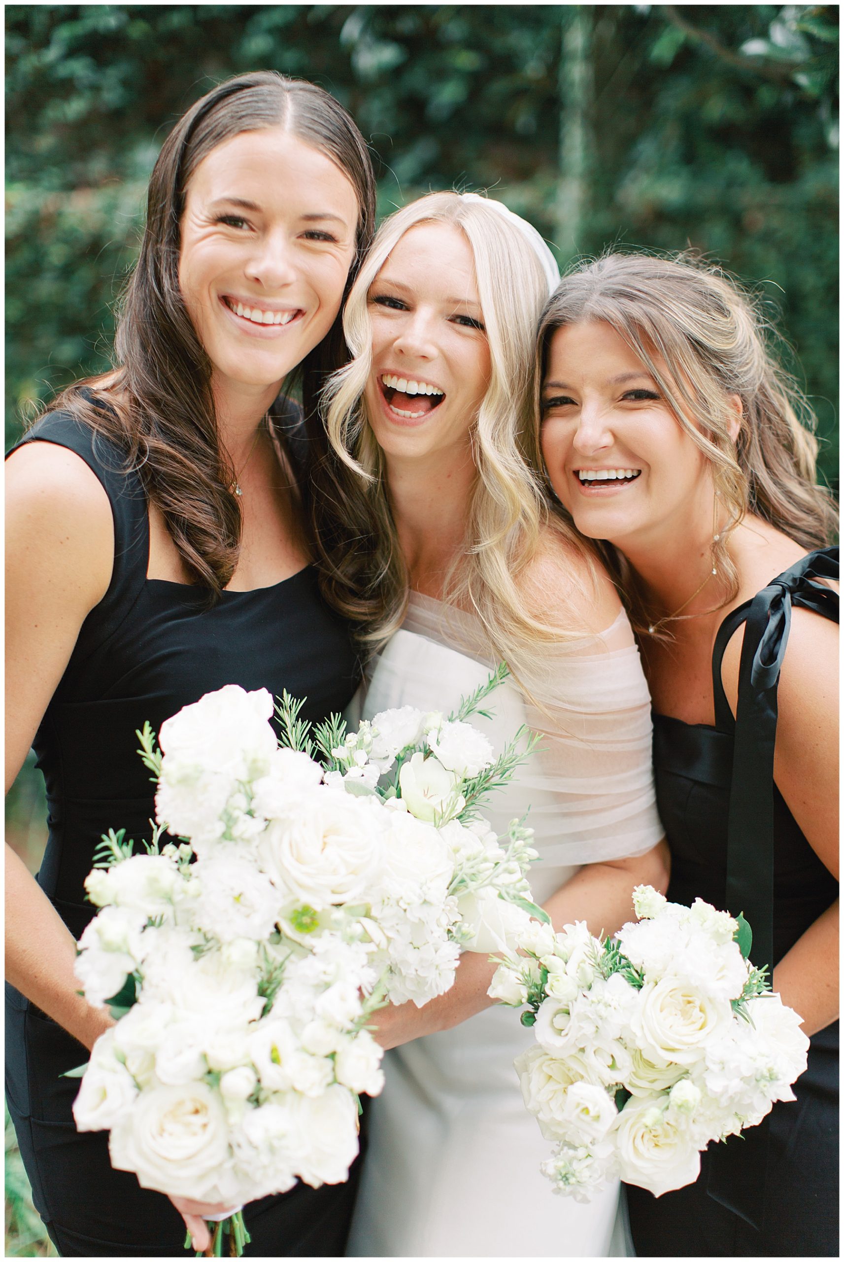 bride laughs with bridesmaids hugging her tight in black dresses 