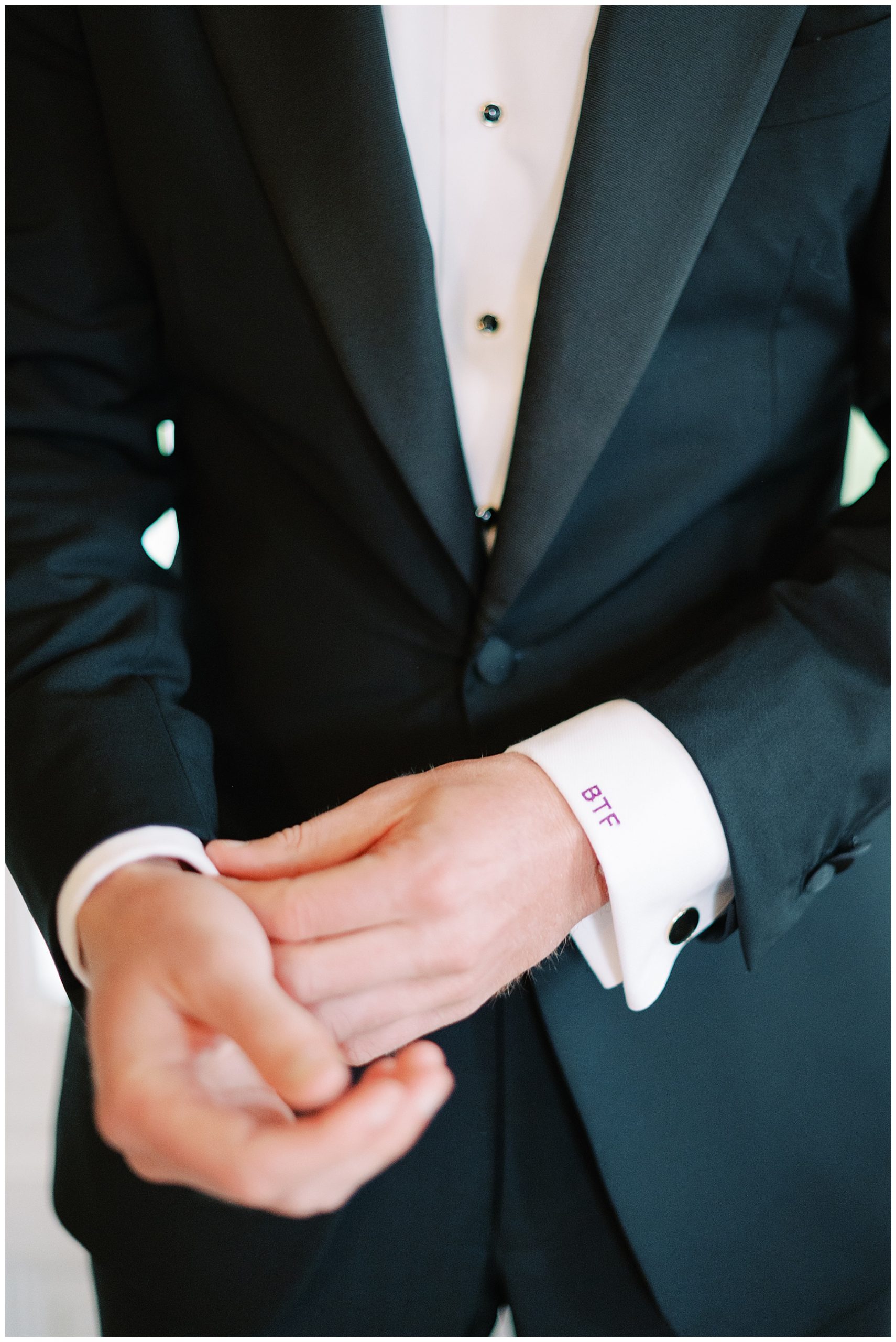 groom adjusts cuffs of white shirt with custom monogram stitched in purple 