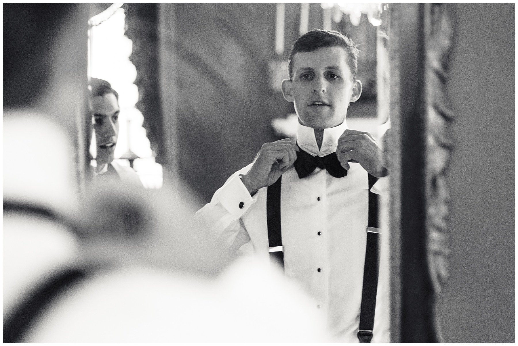 man adjusts bow tie in mirror at the William Aiken House