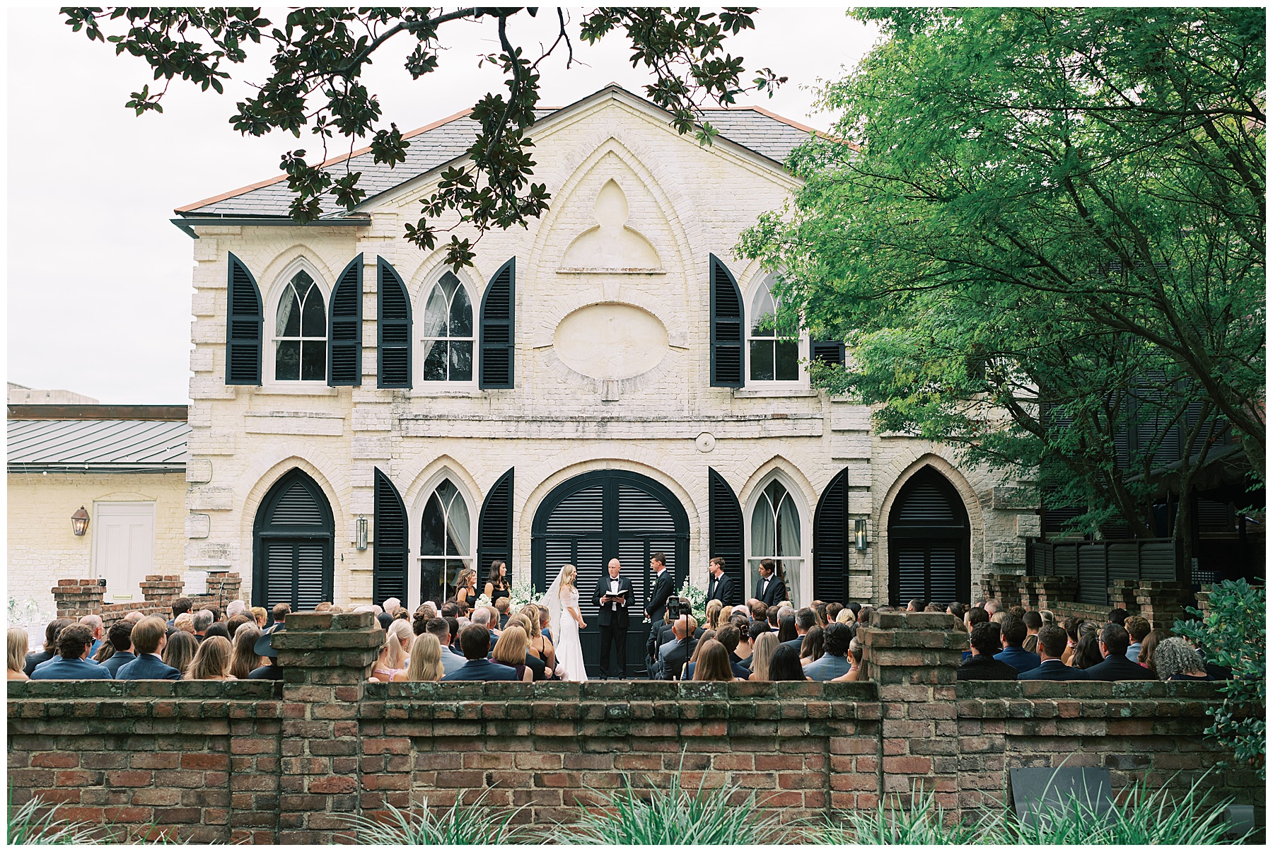 bride and groom stand on patio in front of brick wall exchanging vows at the William Aiken House