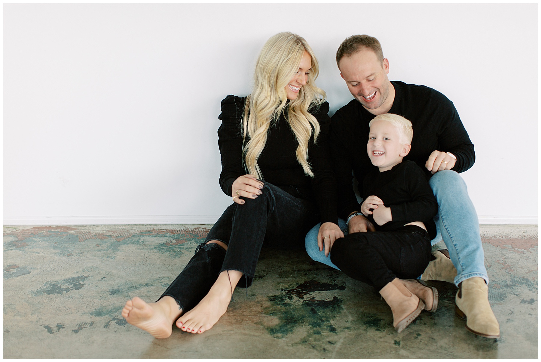 parents laugh with young son on their laps during Charlotte studio family session