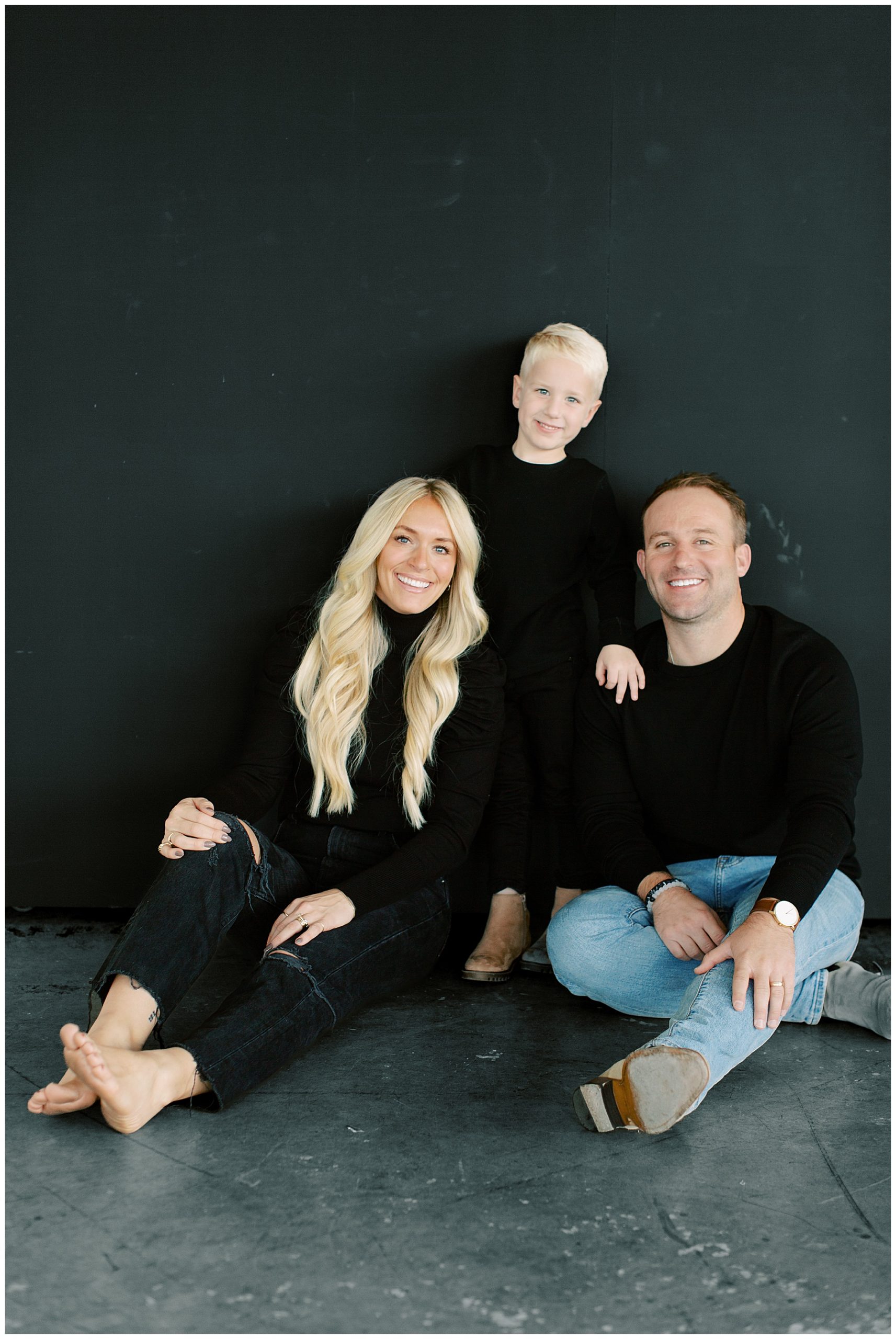 parents in black tops and jeans sit with son between them during Charlotte studio family session