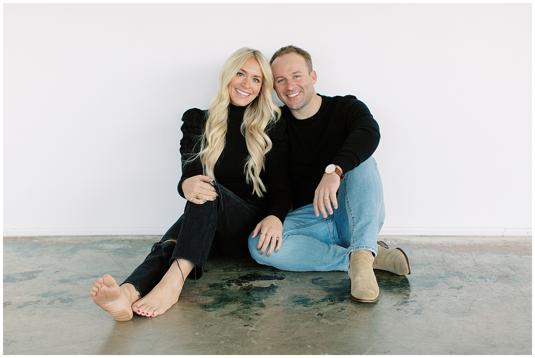 blonde woman snuggles against husband in front of white wall during Charlotte family photos 