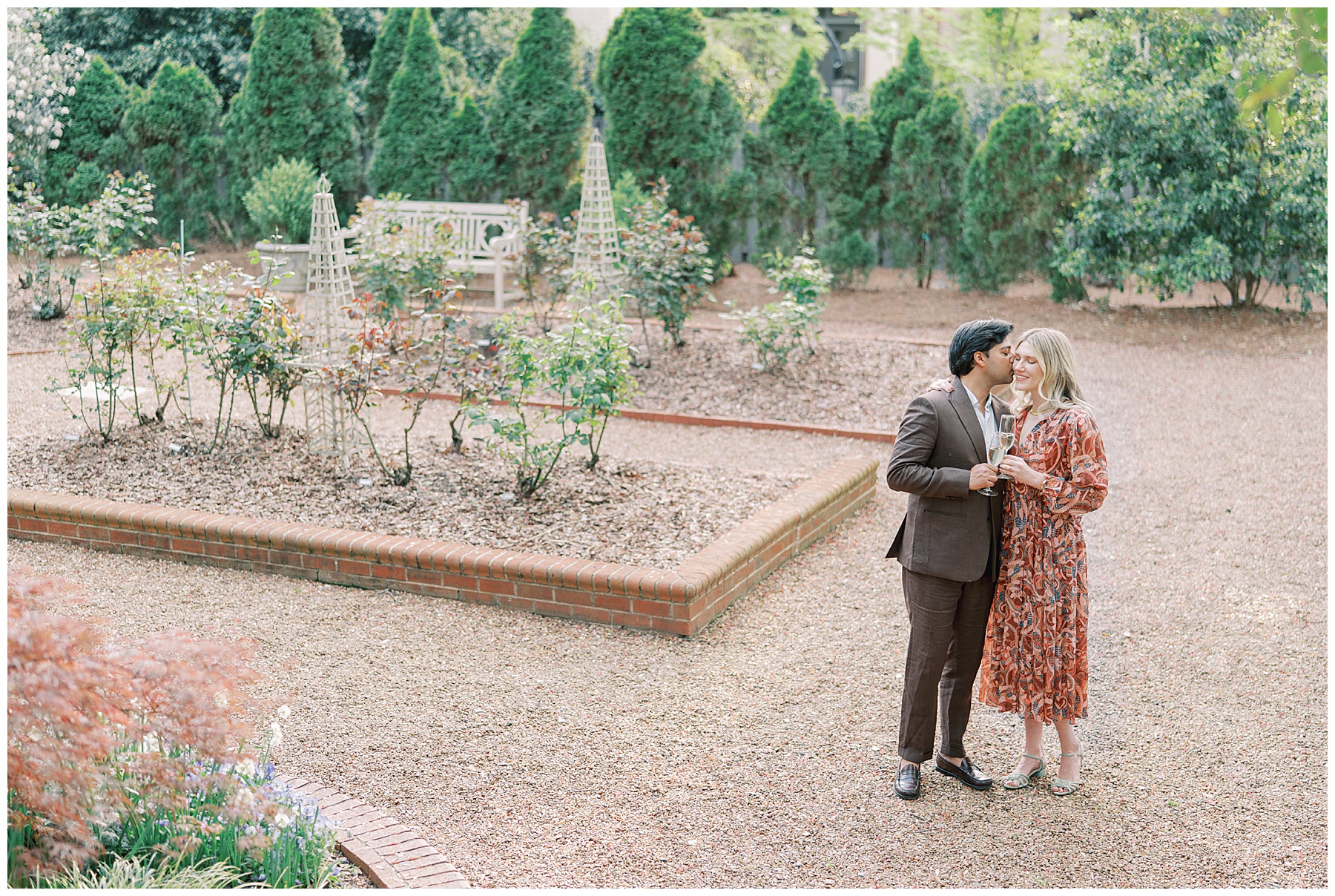 engaged couple toasts champagne glasses in gardens of Duke Mansion