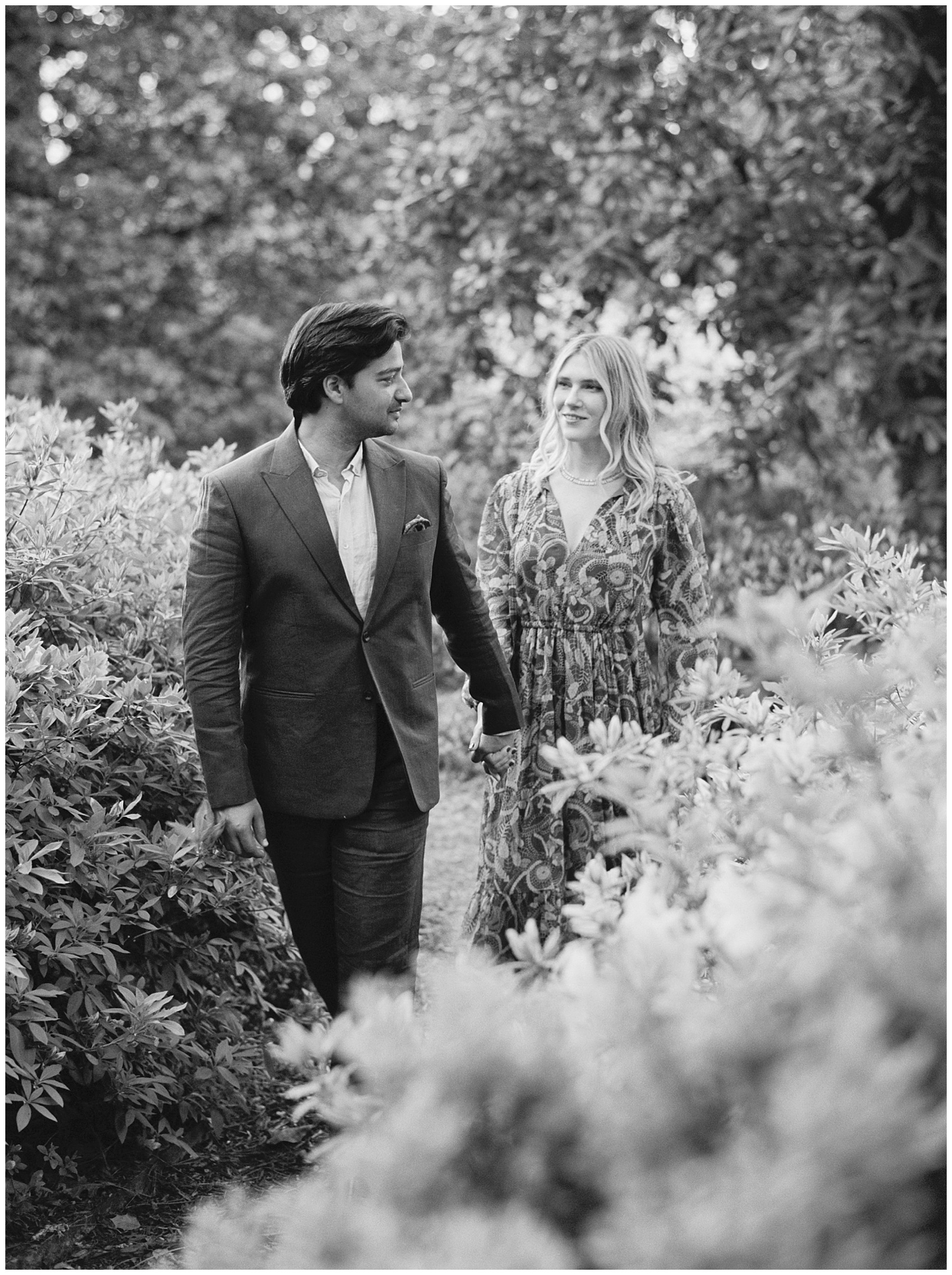 engaged couple holds hands walking through gardens during Duke Mansion engagement session