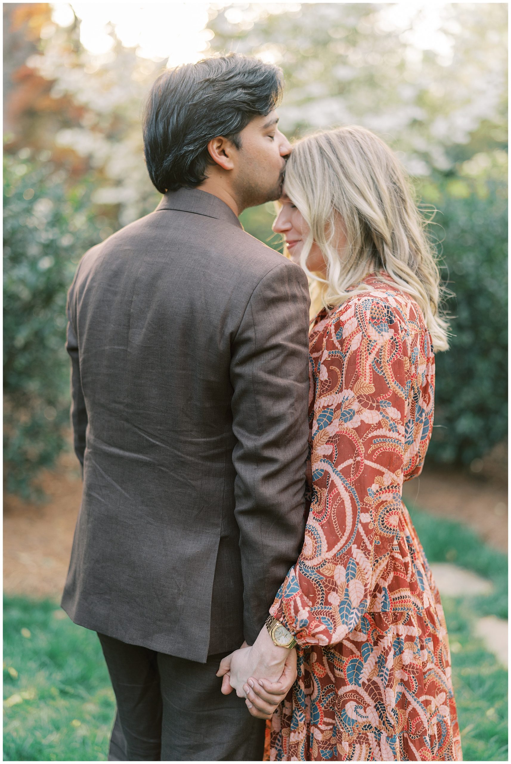 woman holds man's hand while he kisses her forehead in the gardens during Duke Mansion engagement session