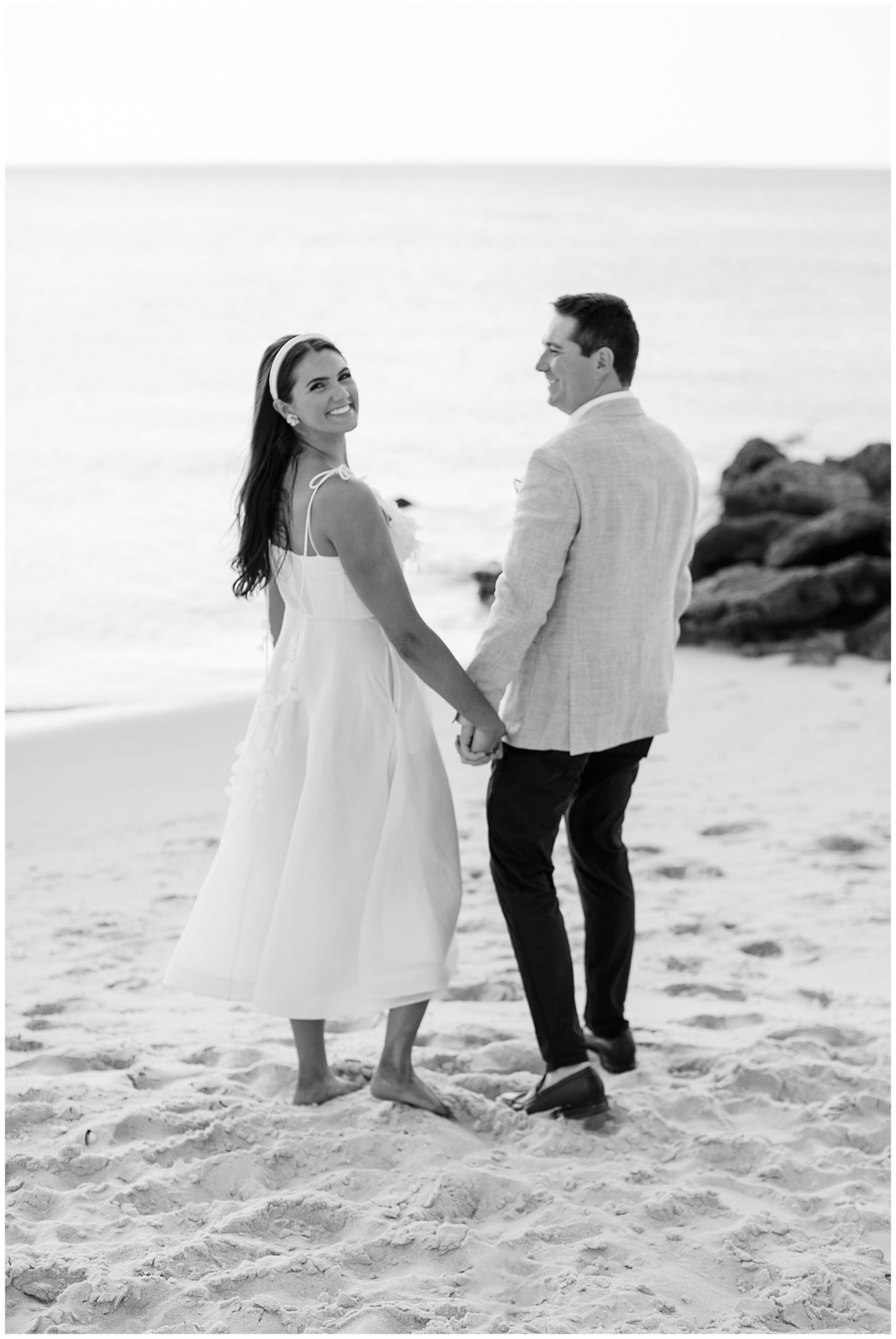 black and white photo of bride and groom holding hands walking on sand in Naples FL