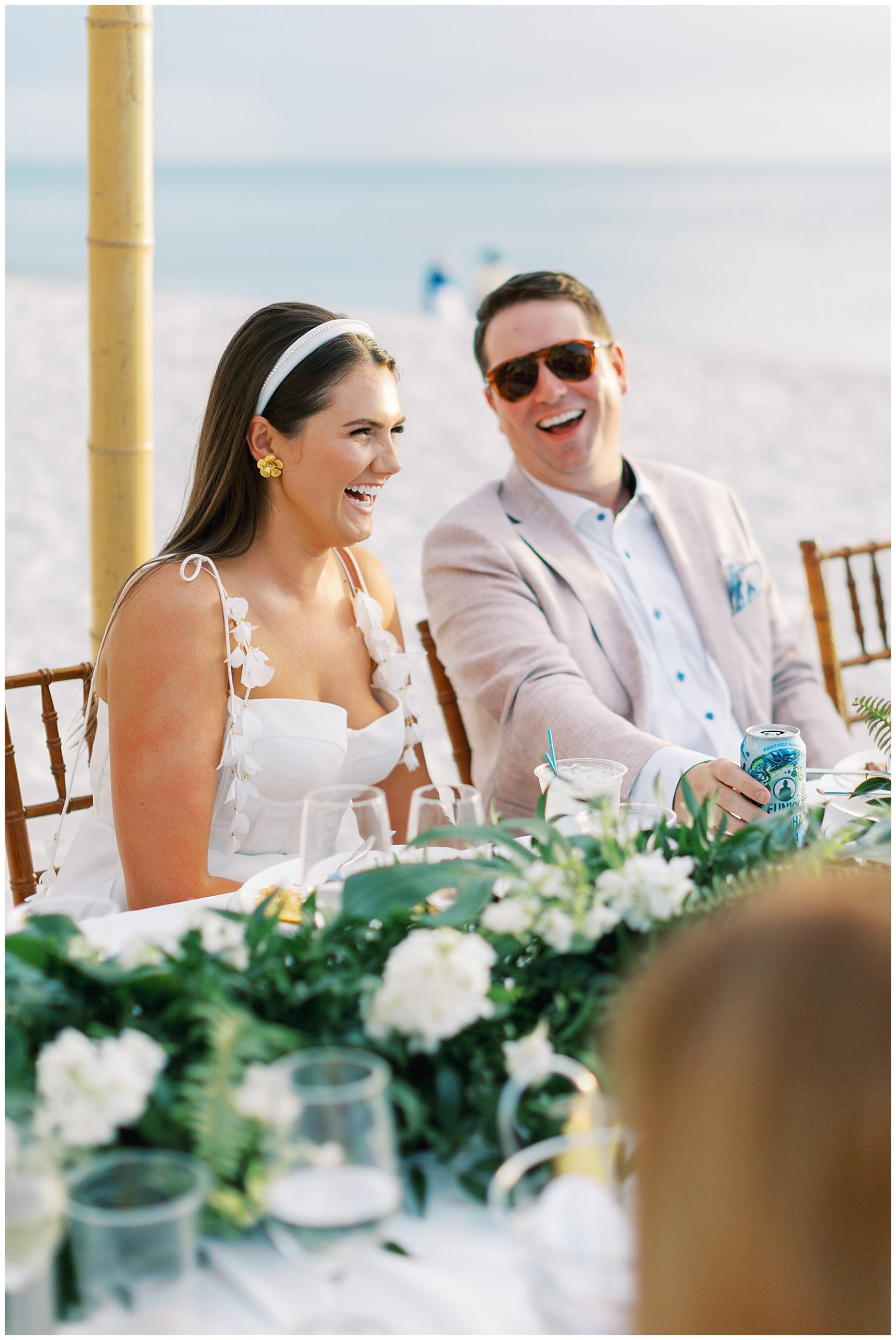 bride and groom laugh sitting on beach during rehearsal dinner in Naples FL