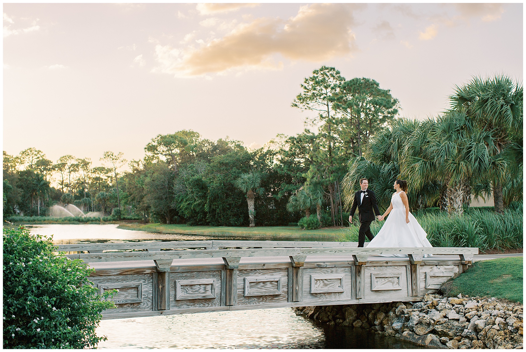 newlyweds hold hands walking across wooden bridge at sunset at Grey Oaks Country Club