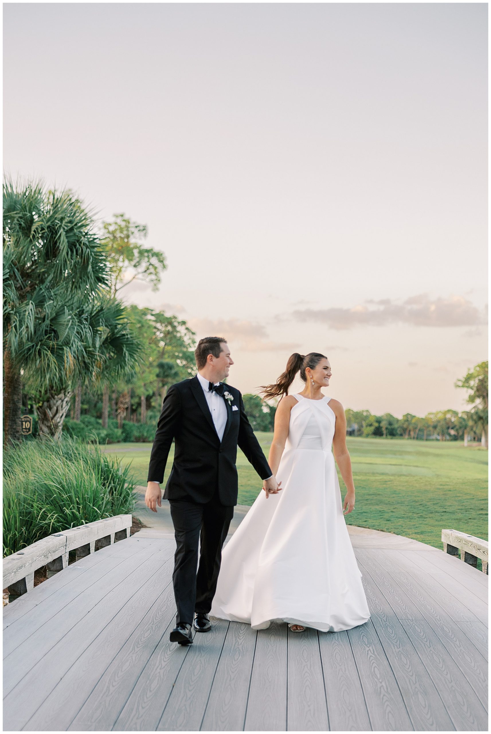 bride and groom hold hands walking over wooden bridge in Naples FL