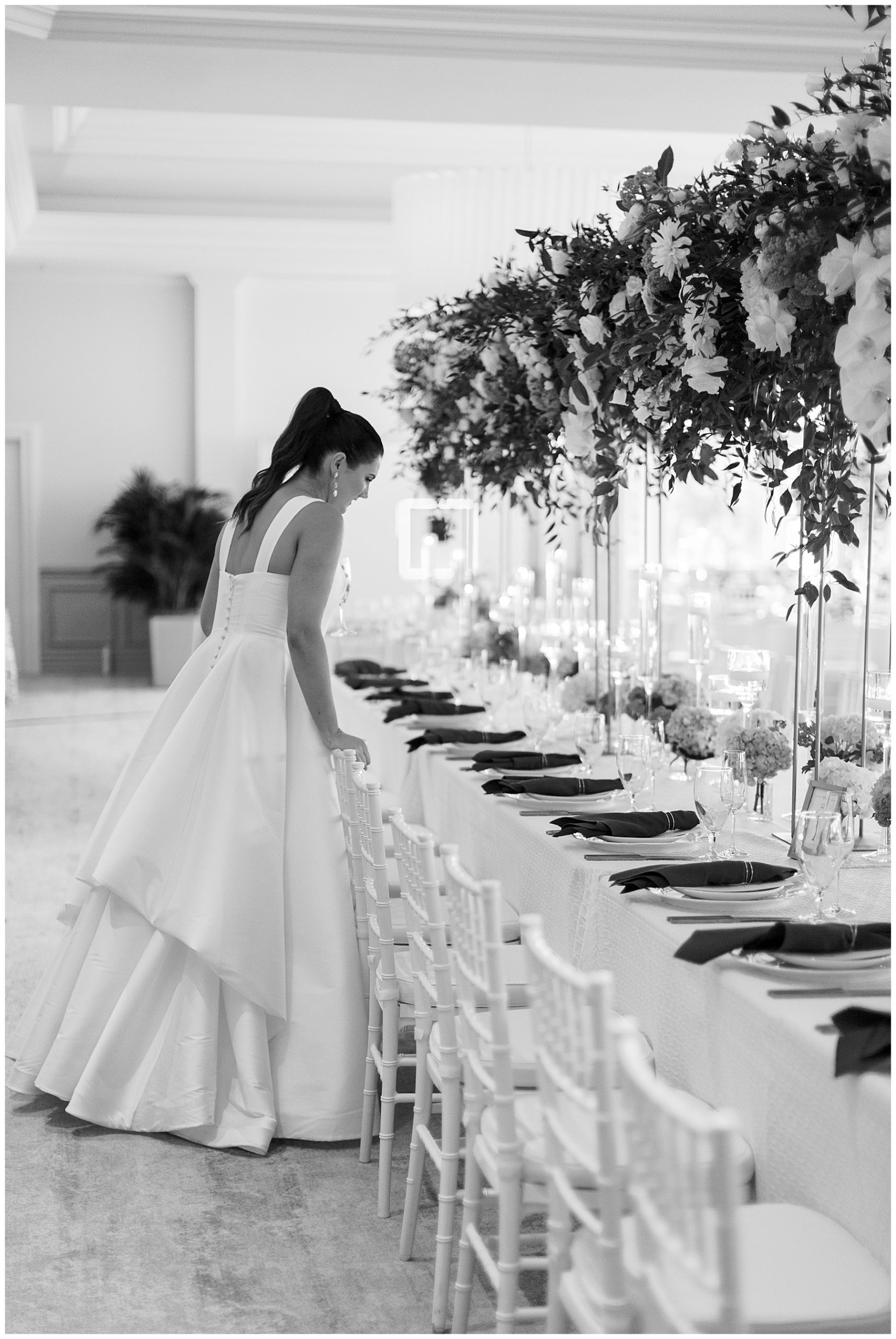 bride looks at place setting leaning over white chivari chairs at Grey Oaks Country Club