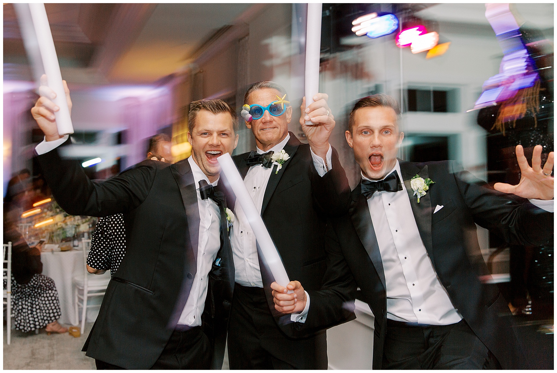 groom and groomsmen dance during reception with glow sticks and funny sunglasses 