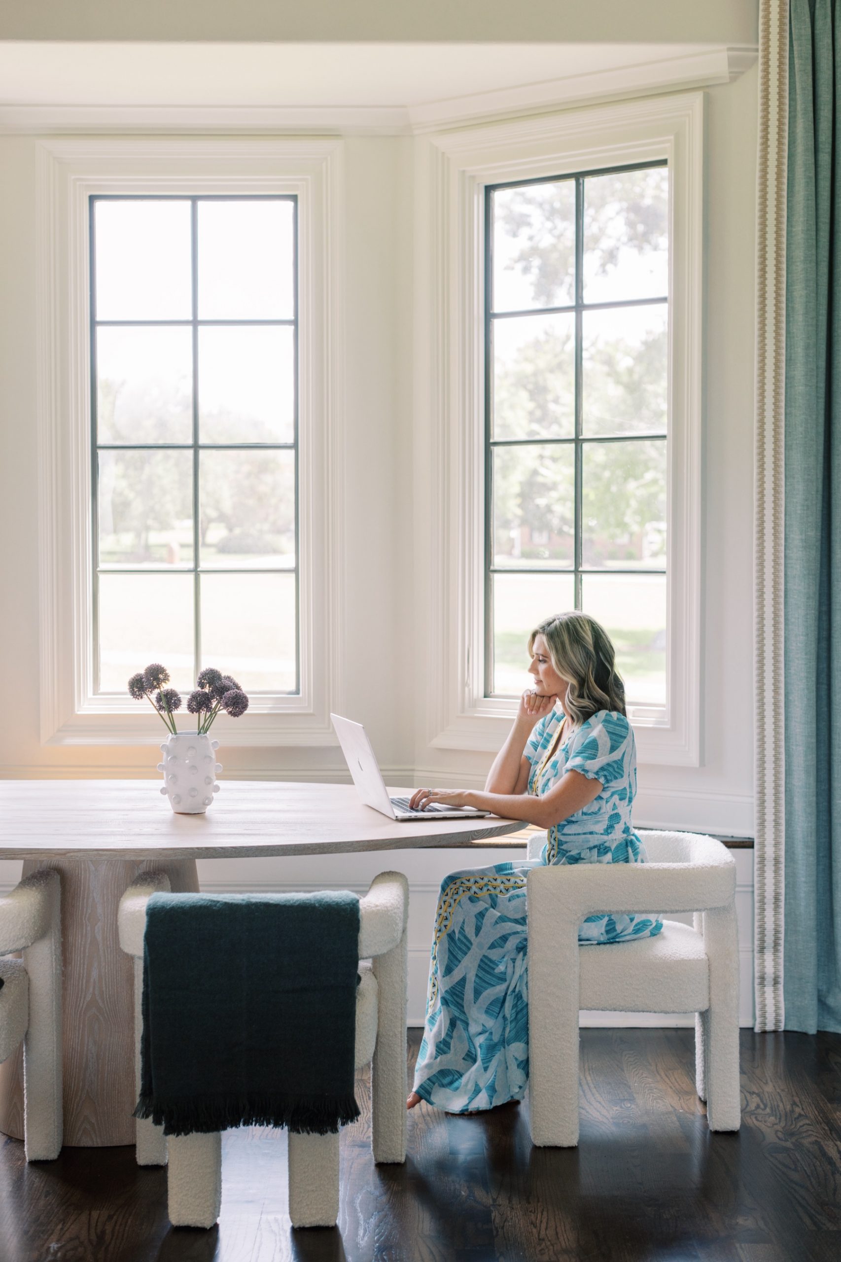 woman sits at kitchen table on laptop during interior photographer branding session in Charlotte NC