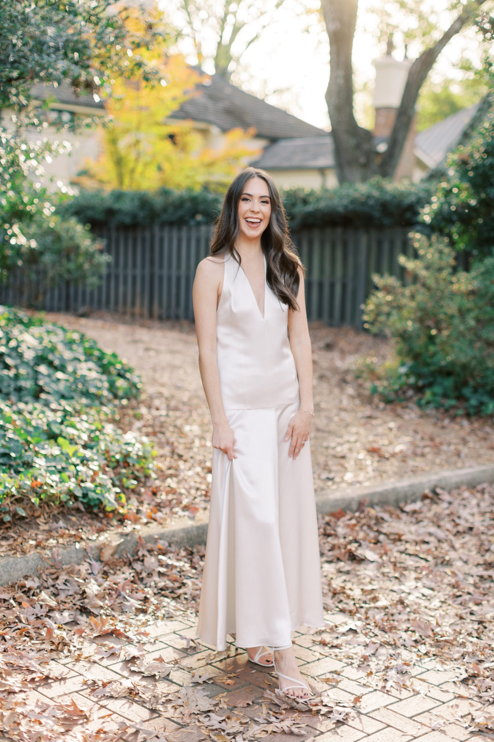 woman poses in satin ivory gown on brick patio covered in leaves at Duke Mansion 