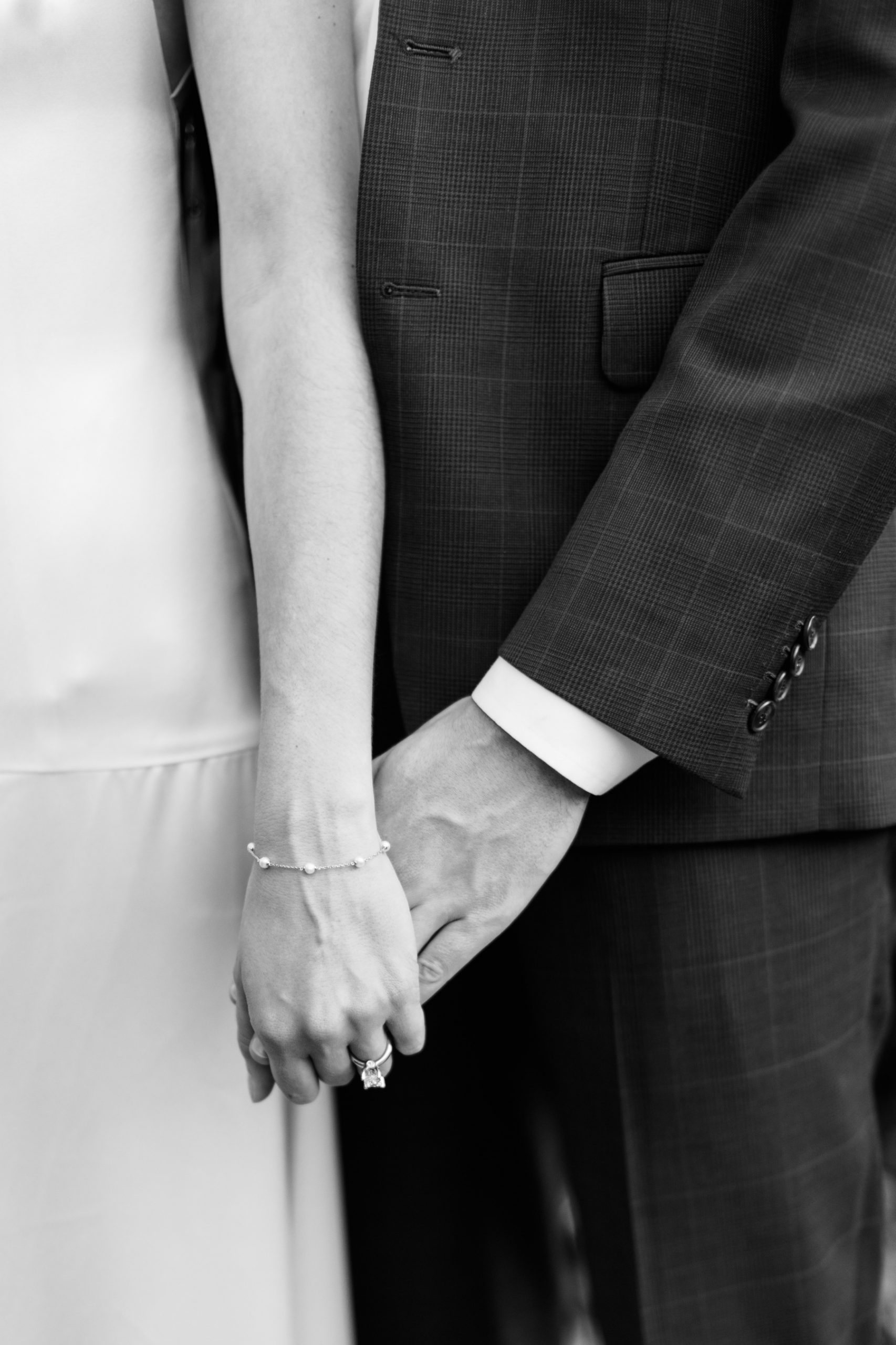 man holds woman's hand with diamond ring and pearl bracelet 