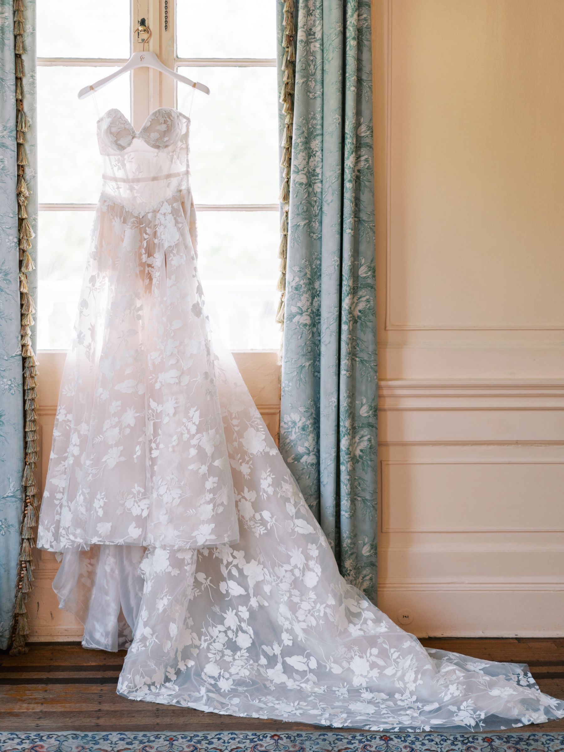Bride's wedding gown hangs in front of window