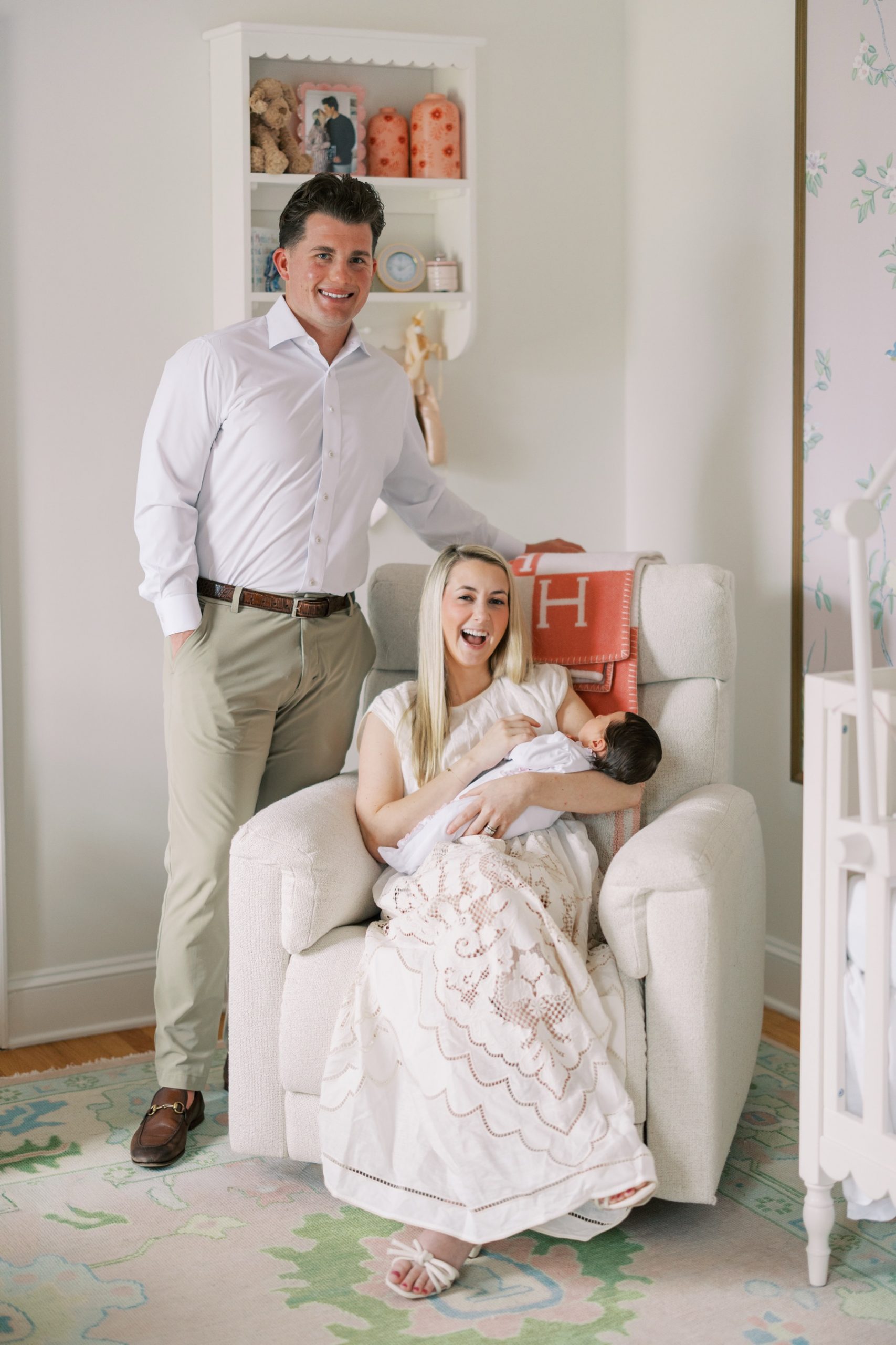 father stands next to his wife and baby girl in the nursery 