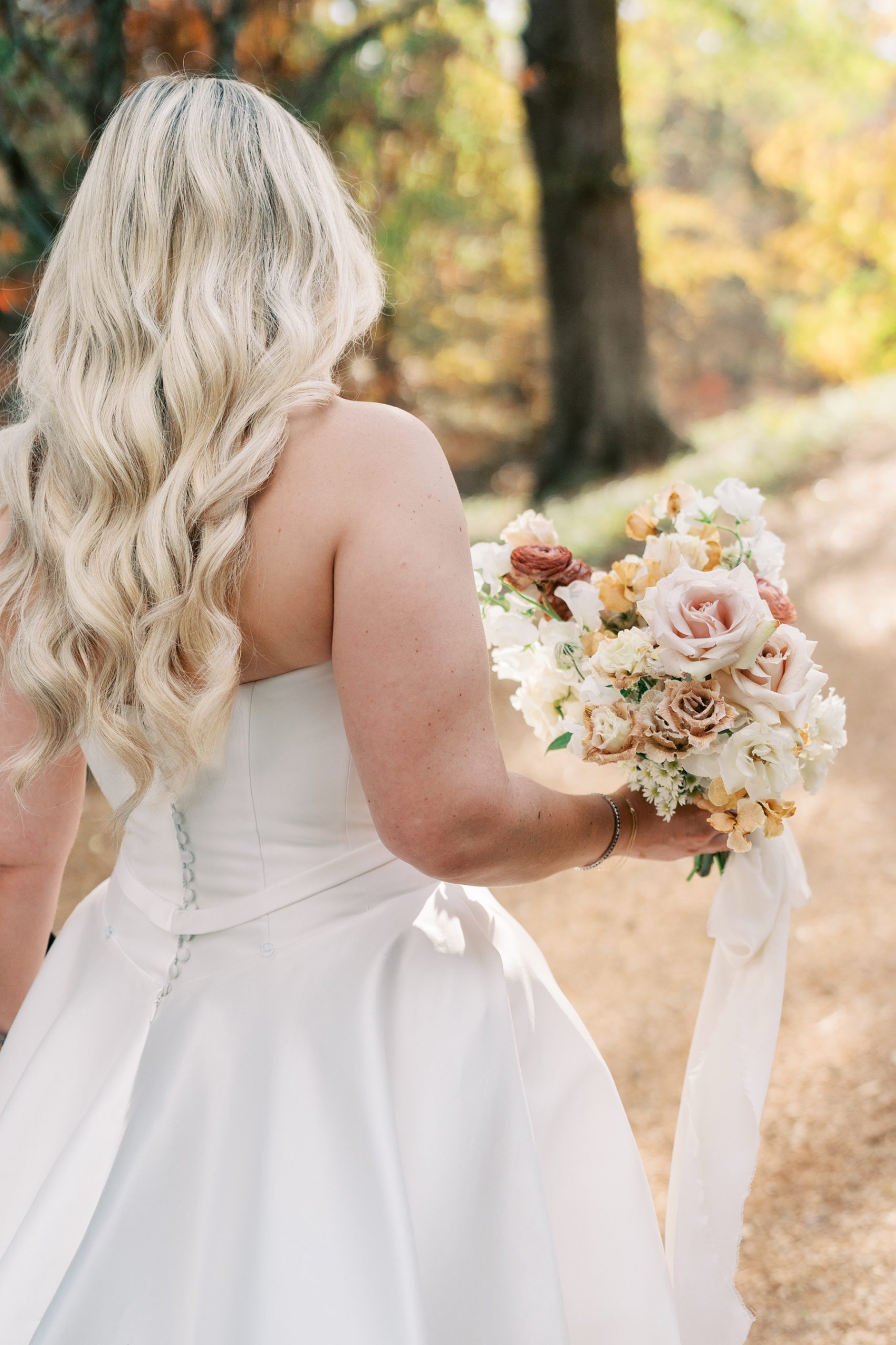 Bride from behind walking outside holding her gorgeous bouquet