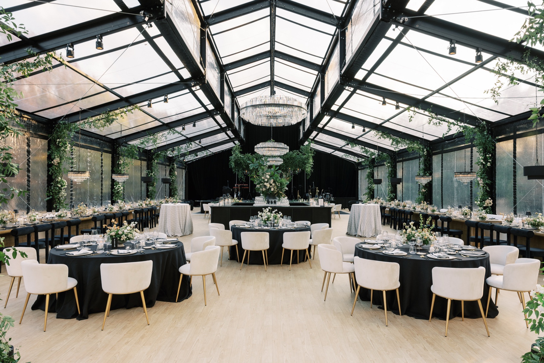 Empty reception area that looks like a large greenhouse with glass ceiling, black tables with white chairs