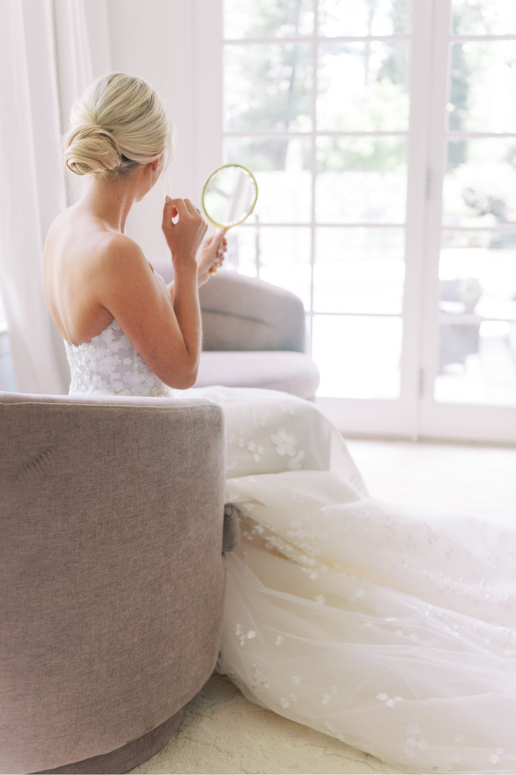 bride touching up her makeup in a small hand held mirror before wedding ceremony