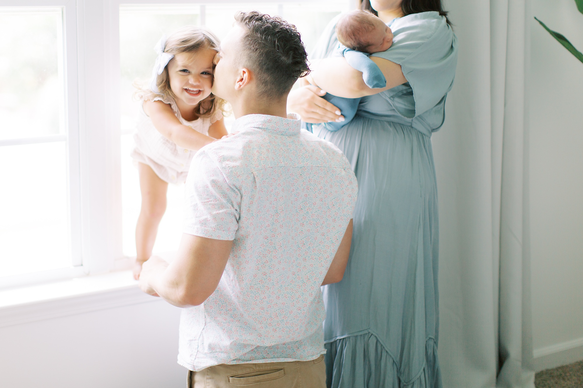 family of four poses by windowsill in Charlotte home during lifestyle newborn photos