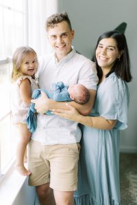 parents pose with two children by window during Charlotte lifestyle newborn session