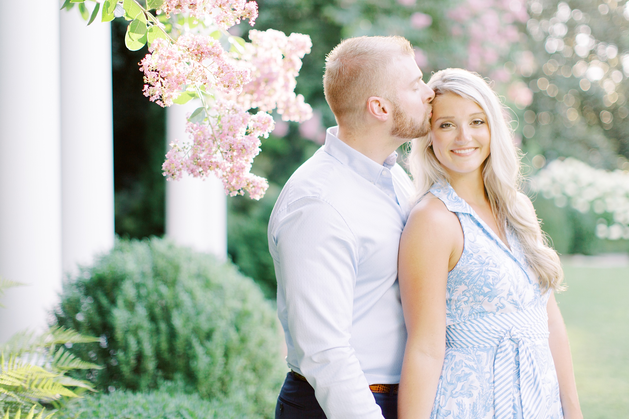 groom kisses bride by pink flowers during Duke Mansion engagement session