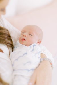 mom holds baby in white and blue blanket during photos at home