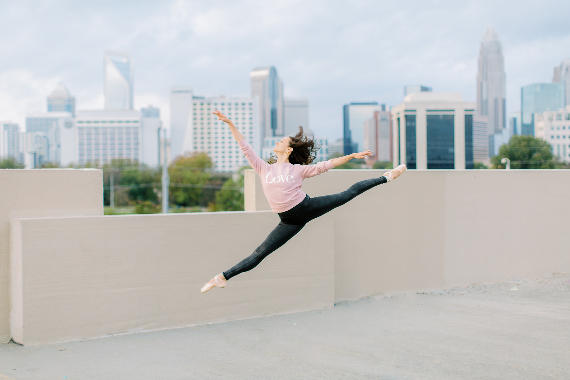 ballerina jumps on parking deck with Charlotte in background