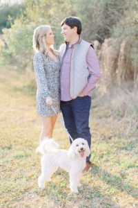 married couple in casual outfits pose with dog on leash during rose garden portraits
