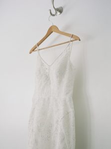 bride's dress with lace details hangs on wooden hanger before Dairy Barn wedding