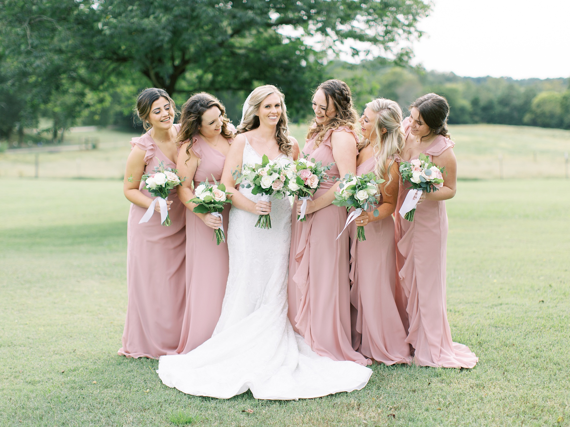 bridesmaids in pink gowns look and smile at bride
