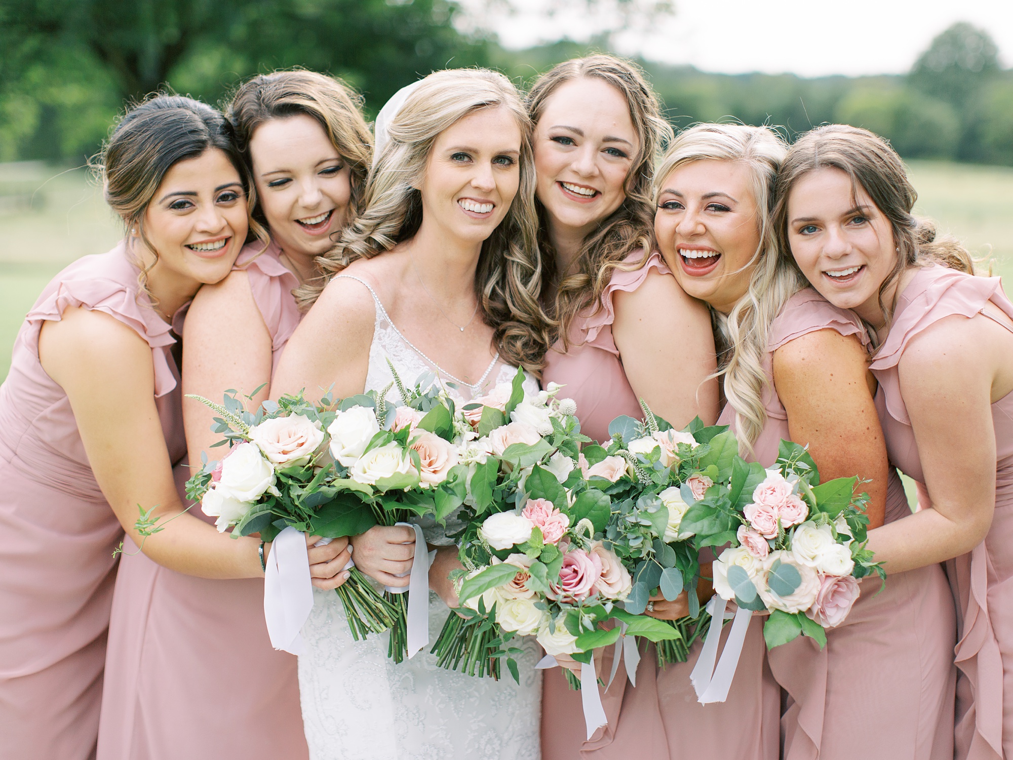 bride poses with bridesmaids in pink gowns outside The Dairy Barn